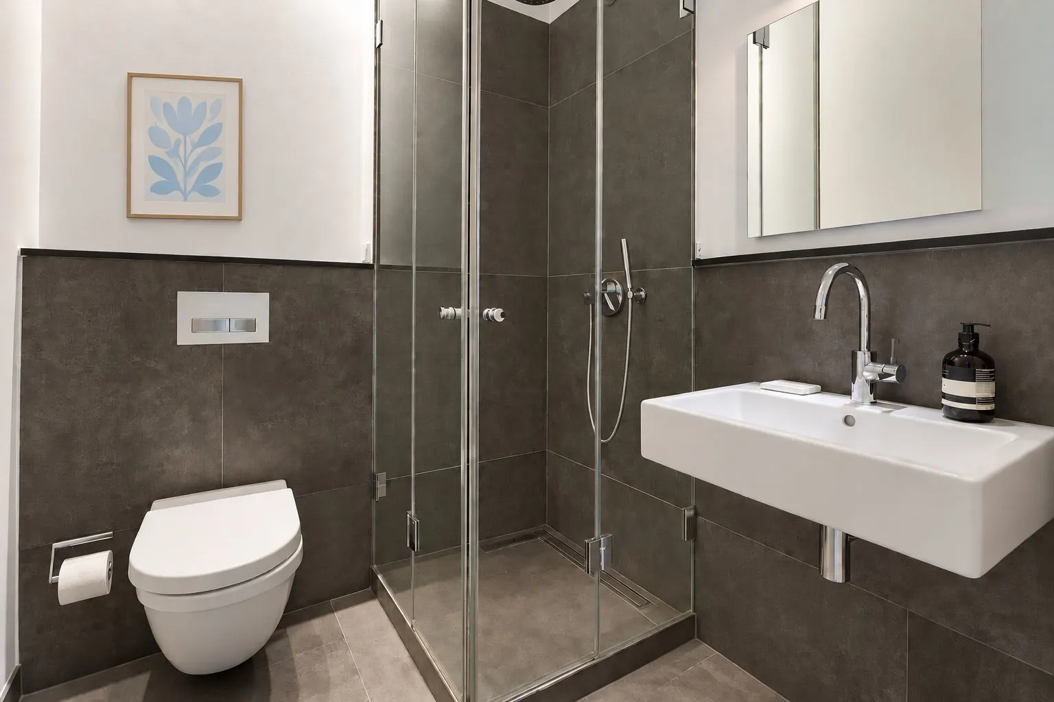 Modernes Bad mit Dusche aus Glas, Wandtoilette, Waschbecken und Spiegel.