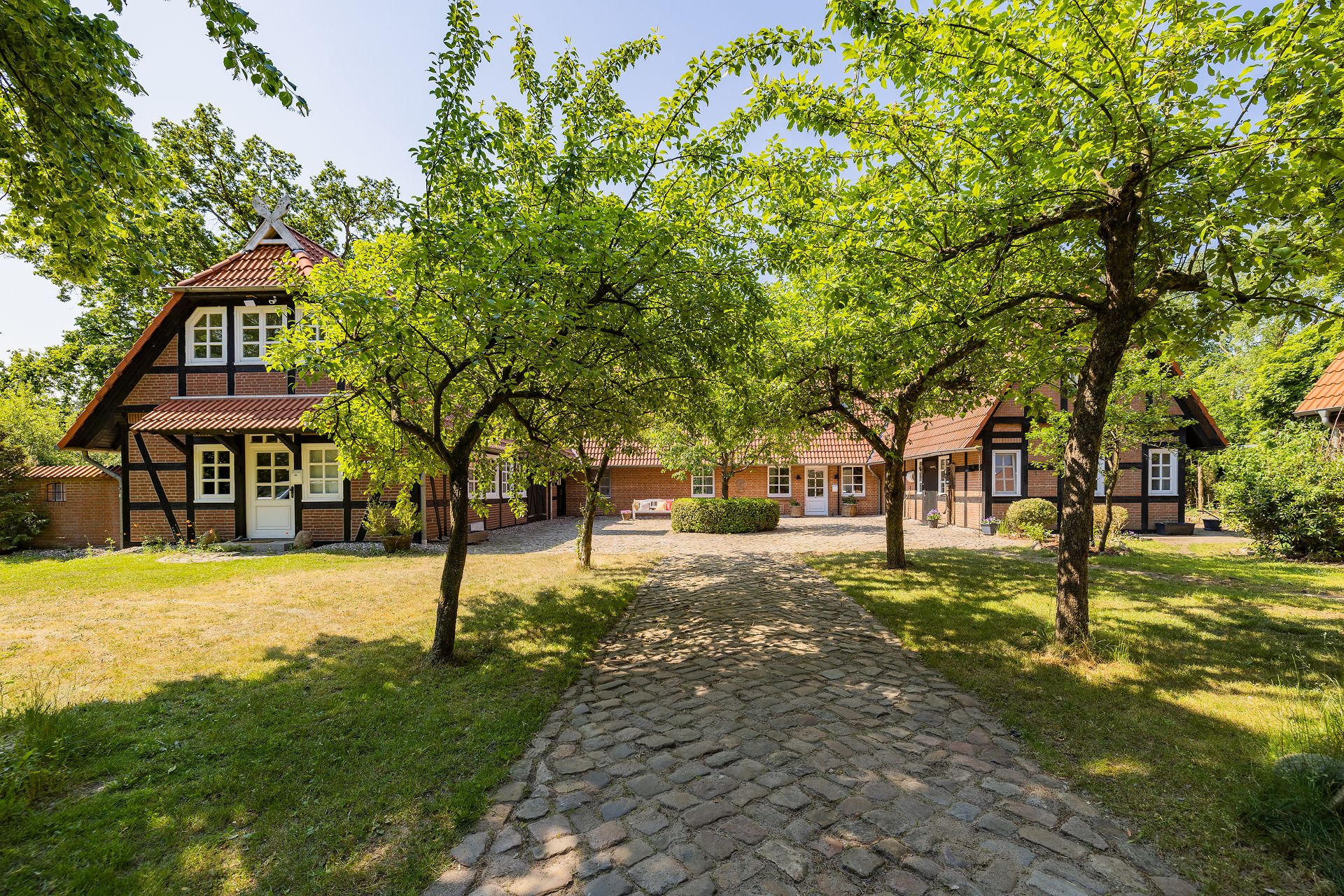 Gepflasterter Weg führt zu Fachwerkhäusern mit roten Dächern und Bäumen im Vorgarten.