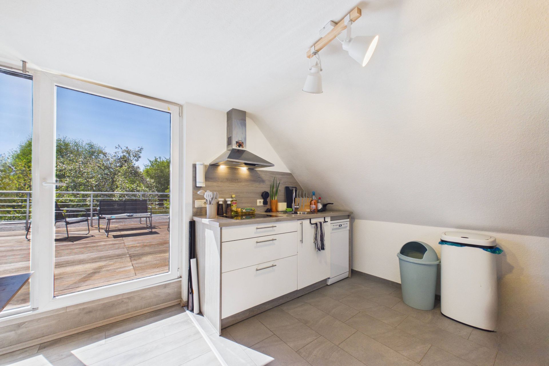 Helle Küche mit Herd, Spüle und Zugang zu einer Terrasse mit Sitzbank.