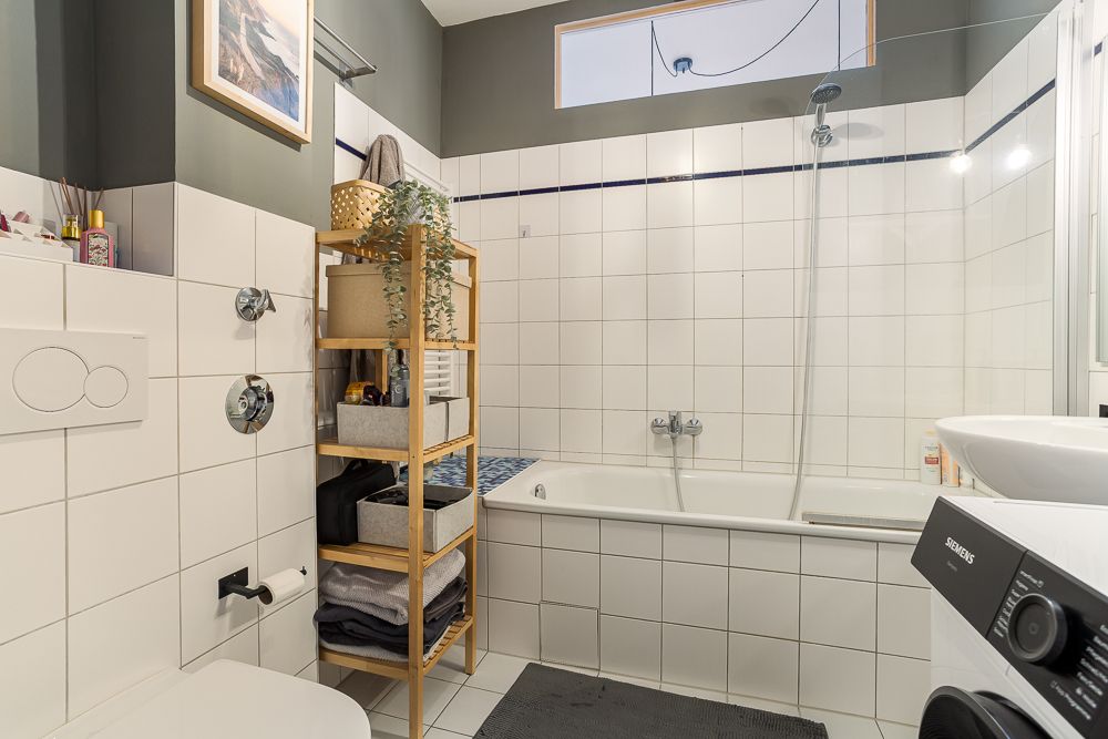 Badezimmer mit Badewanne, Regal, Waschmaschine und Fenster.