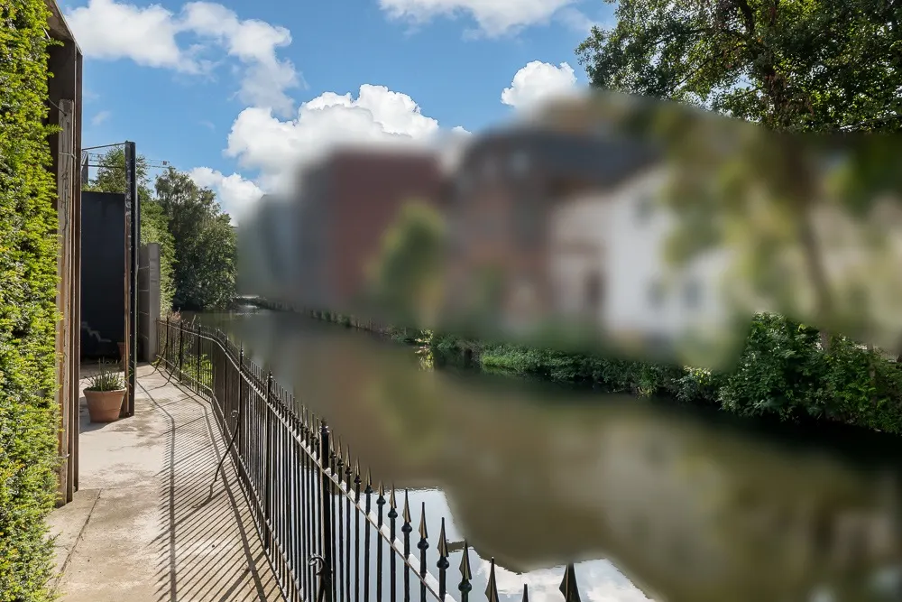 Balkon mit schwarzem Geländer am Wasser, Blick auf Fluss und grüne Bäume.