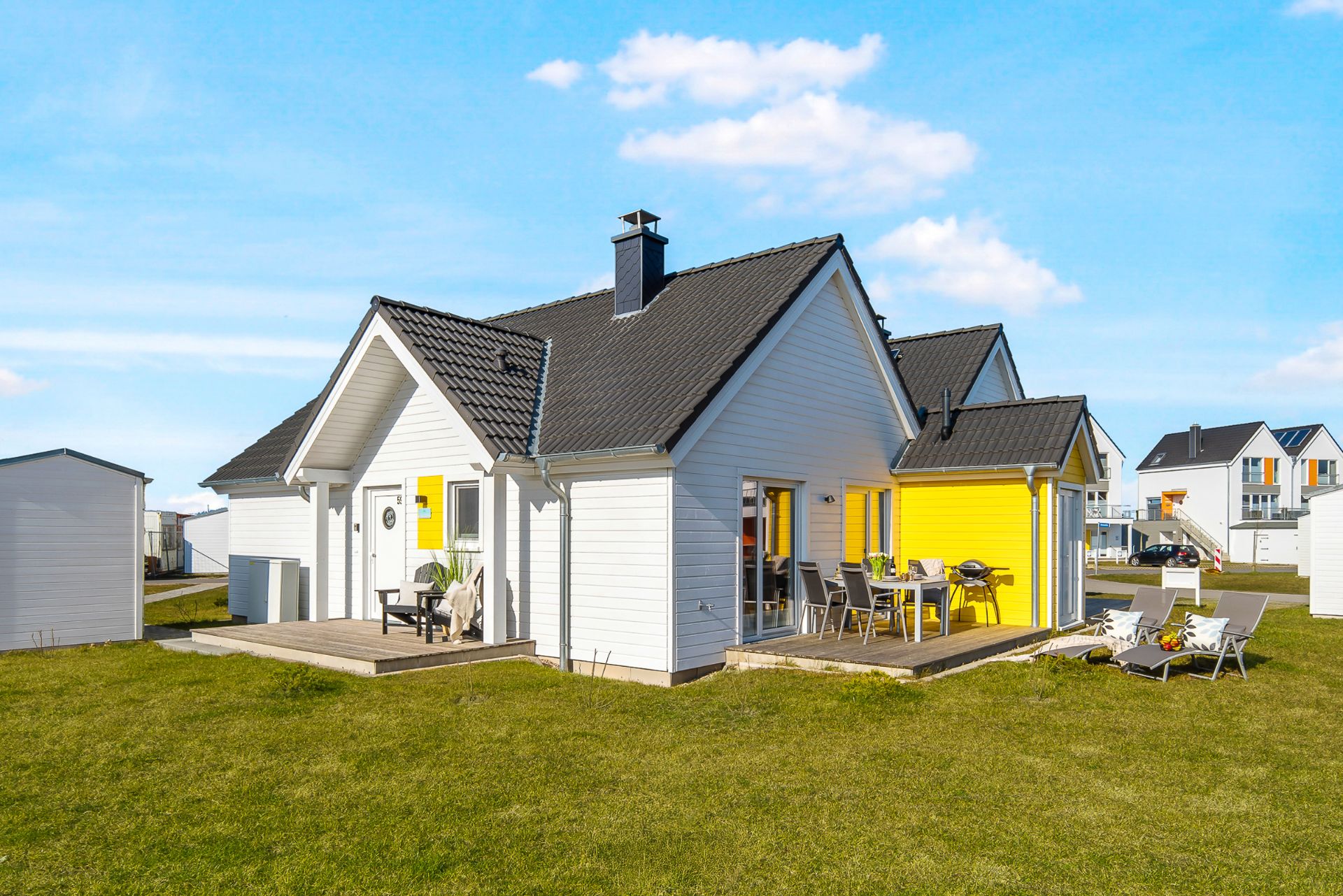 Modernes weißes Einfamilienhaus mit gelben Akzenten, Terrasse und Garten bei sonnigem Wetter.