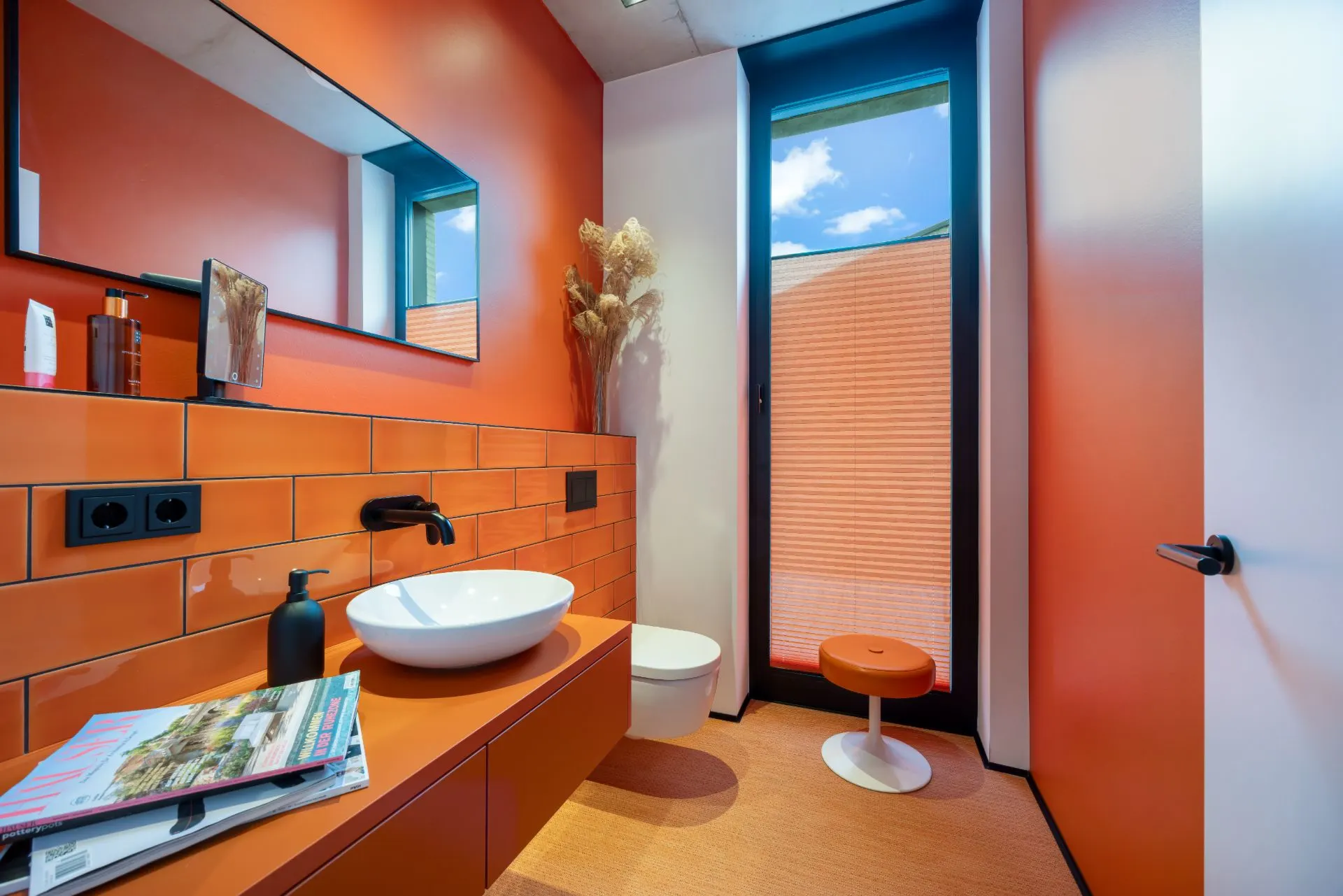 Modernes Badezimmer mit orangen Wänden, Waschbecken, Spiegel, WC und großem Fenster.