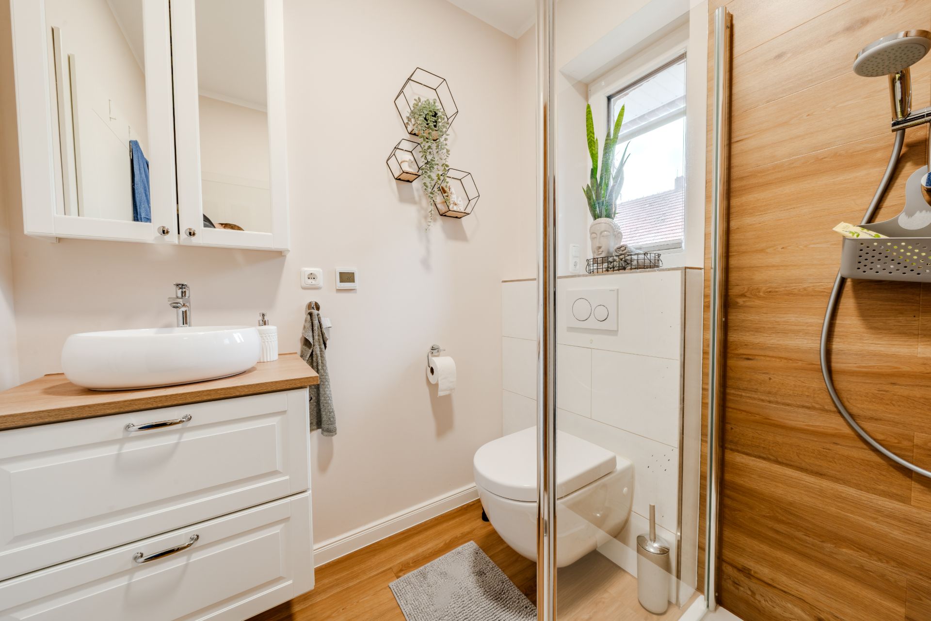 Modernes Badezimmer mit weißem Waschbecken, Toilette, Dusche und Fenster, Holzakzenten und Dekoration.