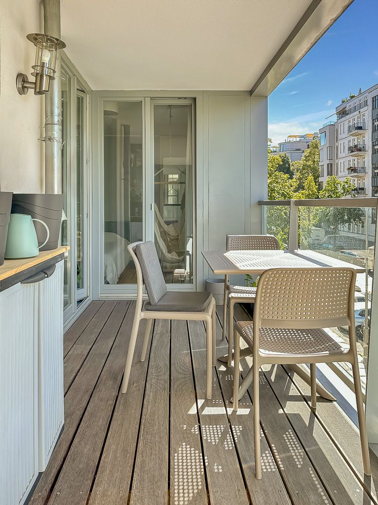 Moderne Balkonterrasse mit Holzboden, Tisch und vier Stühlen, Glasgeländer und Stadtblick.