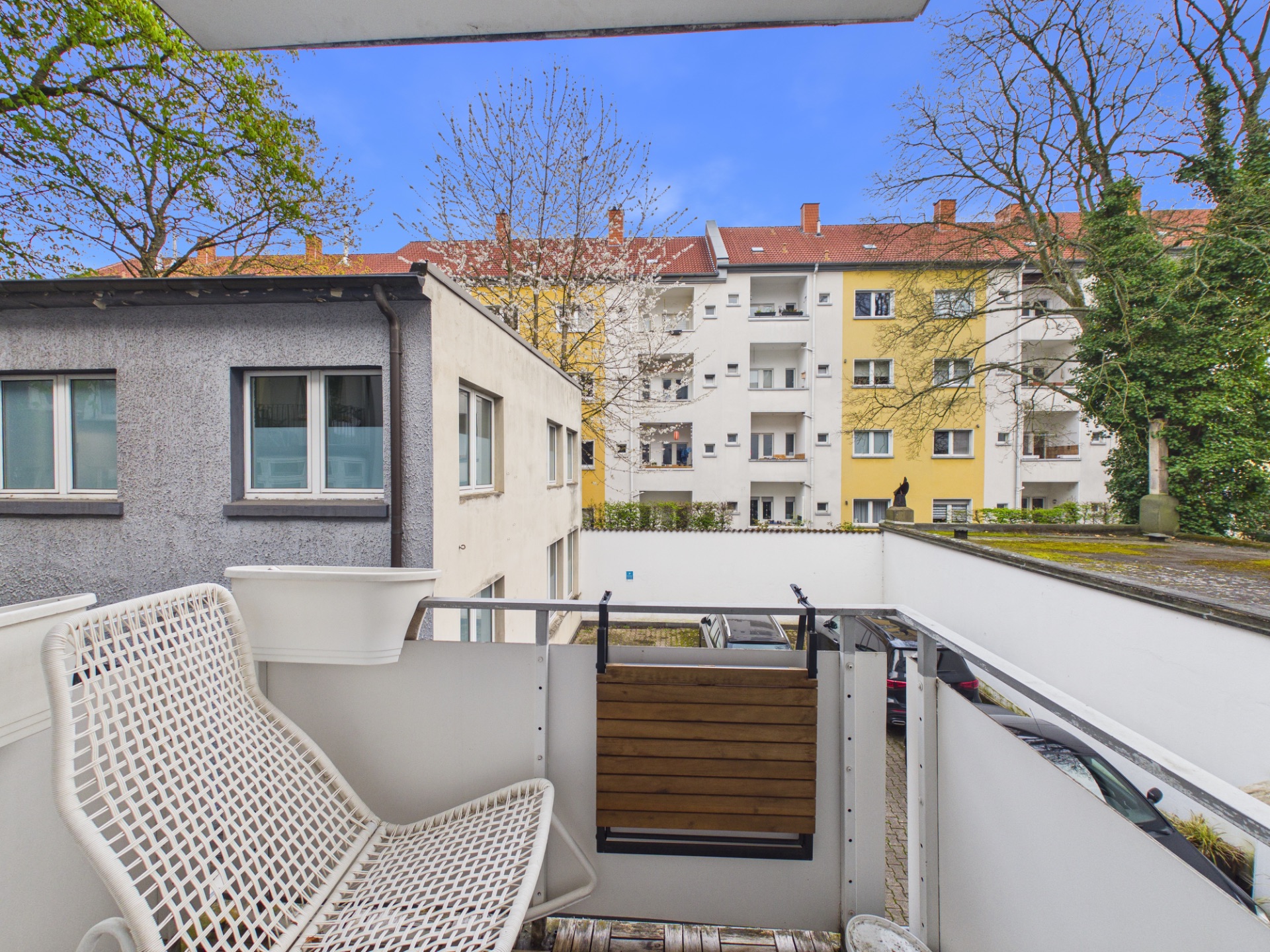 Balkon mit weißem Stuhl, Blick auf Nachbarhäuser und Bäume.