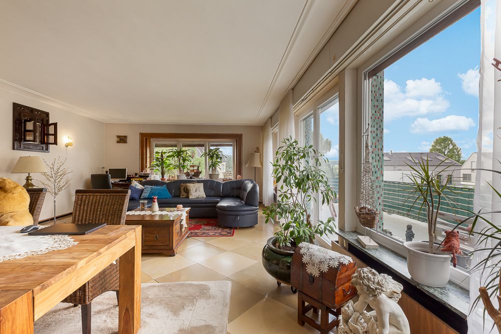 Helles Wohnzimmer mit großen Fenstern, Pflanzen, Sofa und Holzmöbeln.