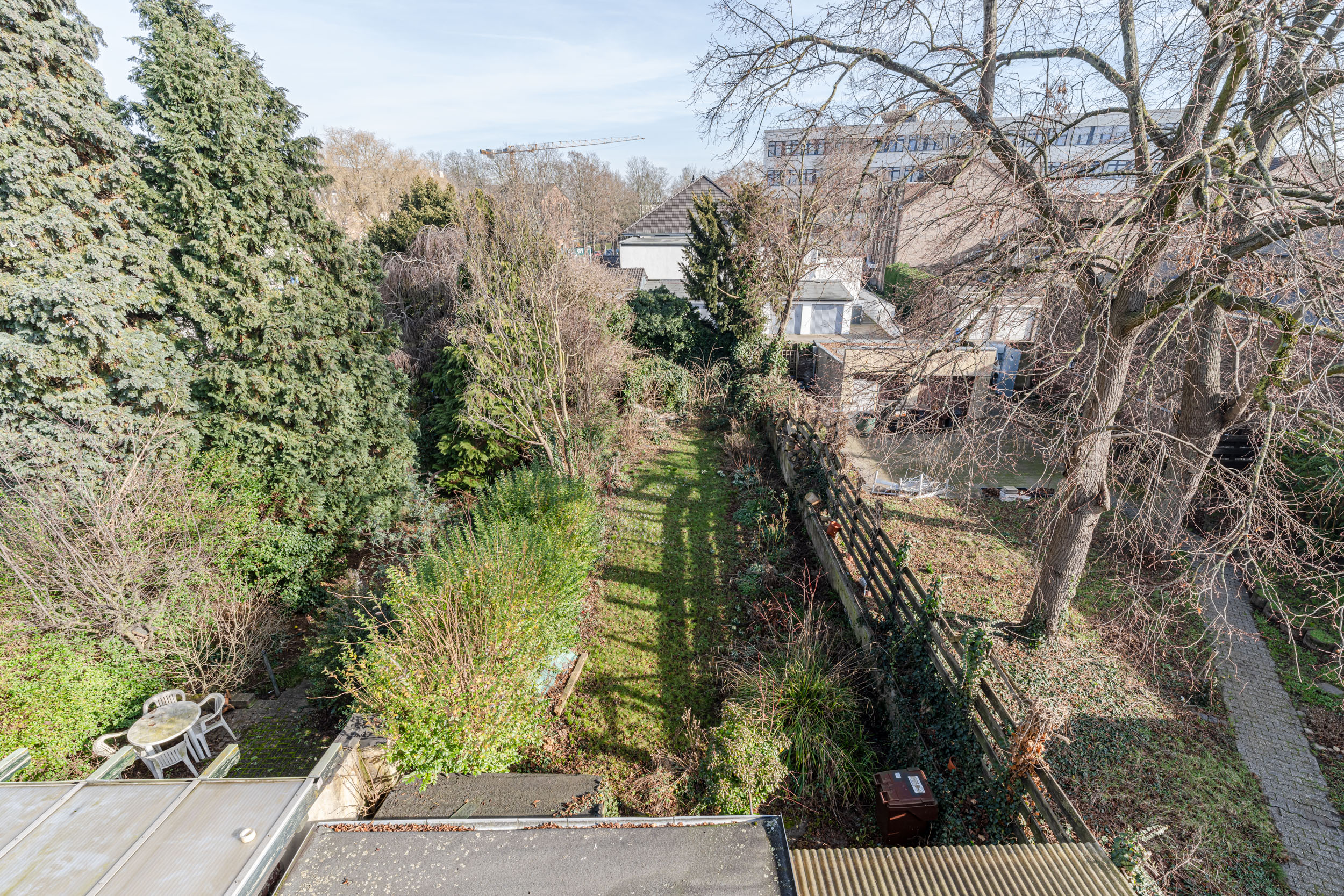 Blick auf einen großen Garten mit Bäumen, Sträuchern und einer kleinen Sitzgruppe in der Ecke.