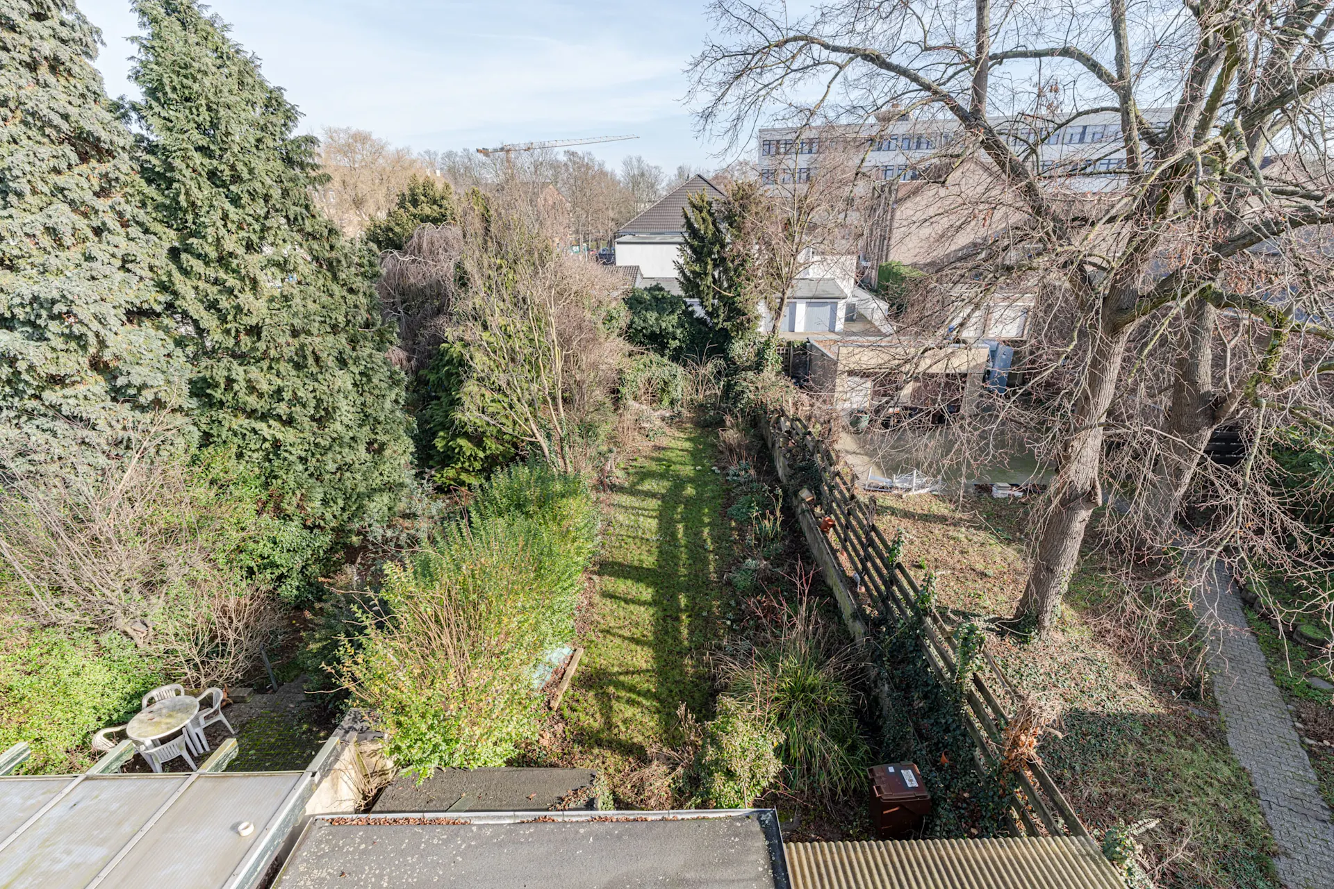 Blick auf einen großen Garten mit Bäumen, Sträuchern und einer kleinen Sitzgruppe in der Ecke.