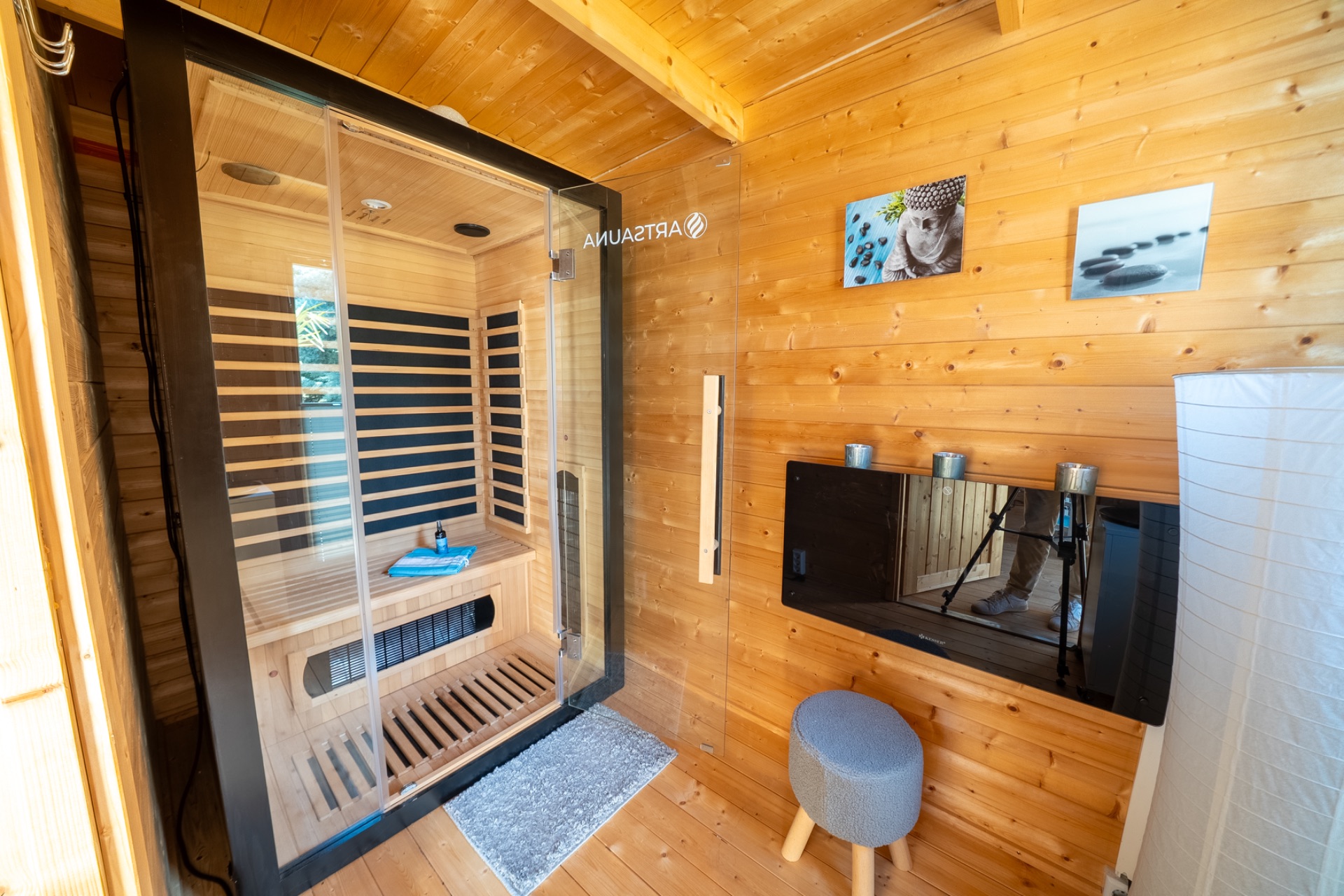 Holzraum mit moderner Sauna, Hocker, Wandbildern und kleinem Wandregal mit Kerzen.