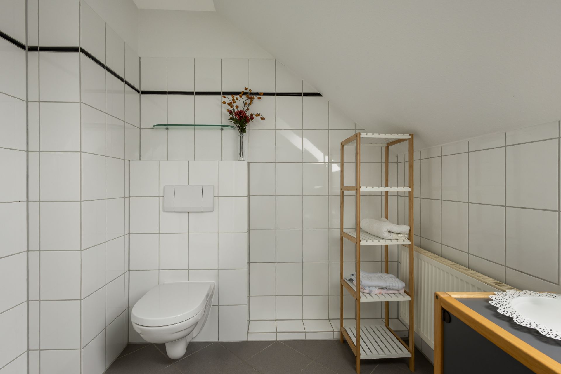 Modernes Badezimmer mit Wandtoilette, Regalen und weißen Fliesen.