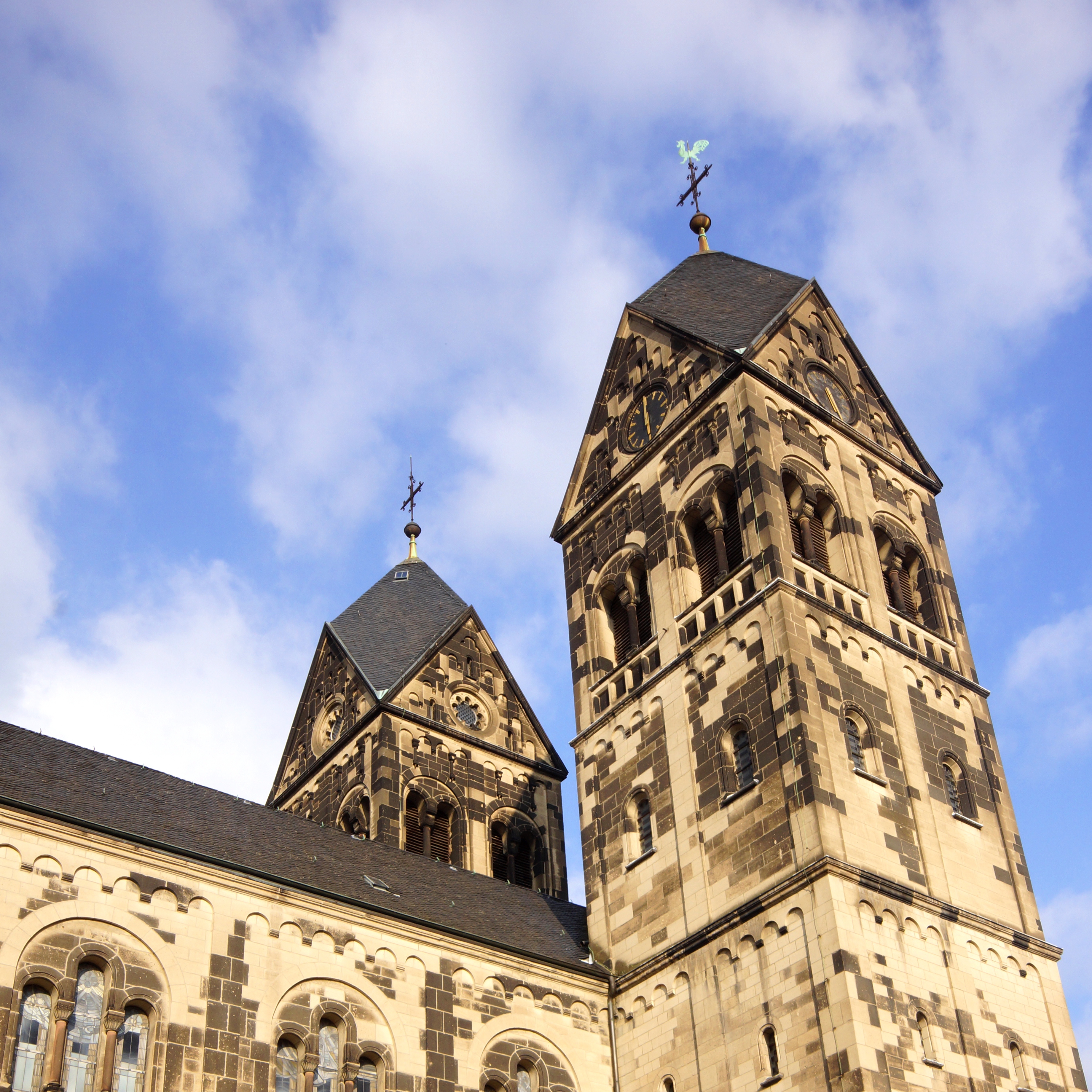 Zwei große Kirchtürme aus Stein mit vielen Fenstern vor blauem Himmel.