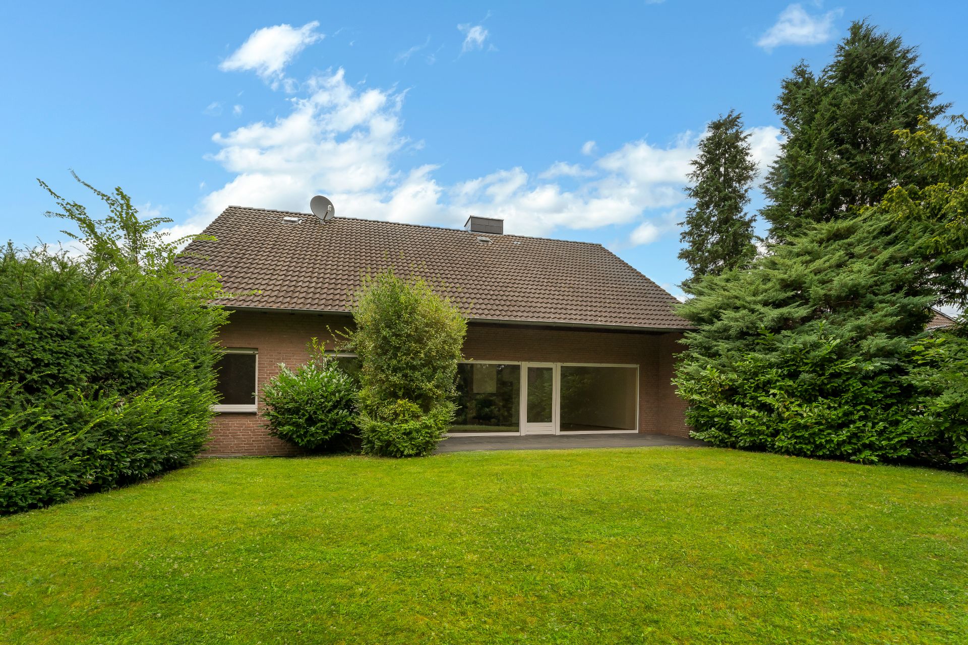 Einfamilienhaus mit großem Garten, Rasenfläche und umgebenden Büschen und Bäumen.