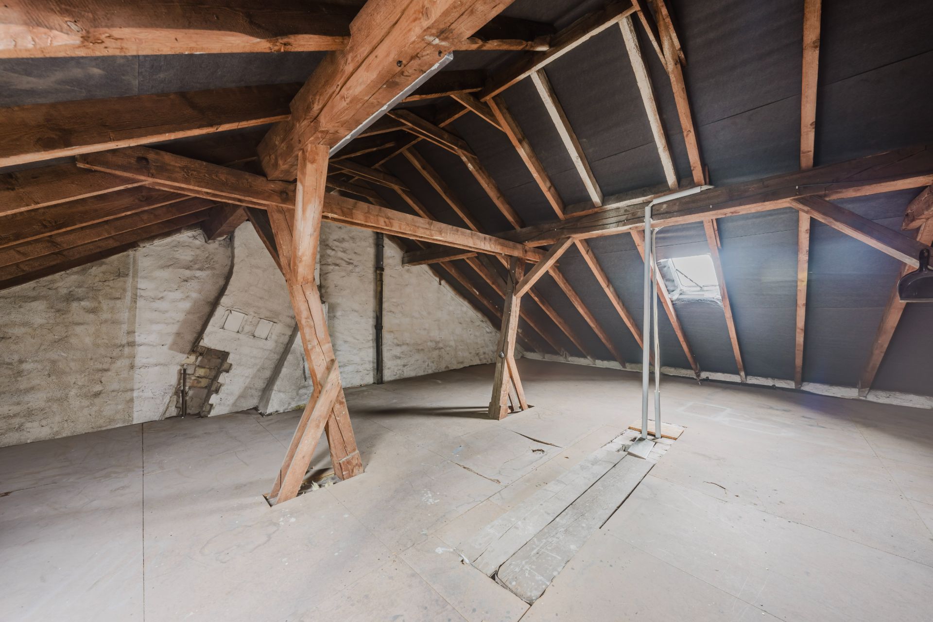 Dachboden mit Holzbalken, Dachfenster und unverputzten Wänden.