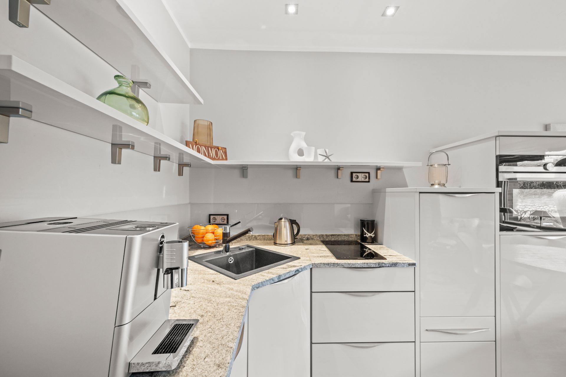 Moderne Küche mit weißer Einrichtung, Kaffeemaschine, Spüle, Herd und offenen Regalen.