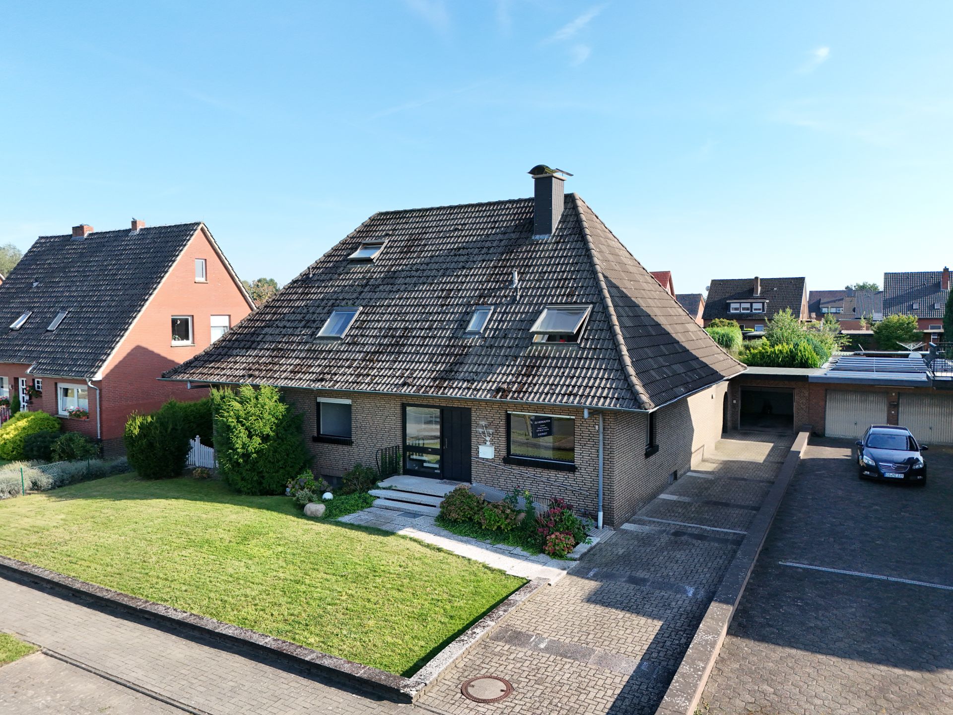 Einfamilienhaus mit dunkel gedecktem Dach, Vorgarten und Einfahrt bei klarem Himmel.