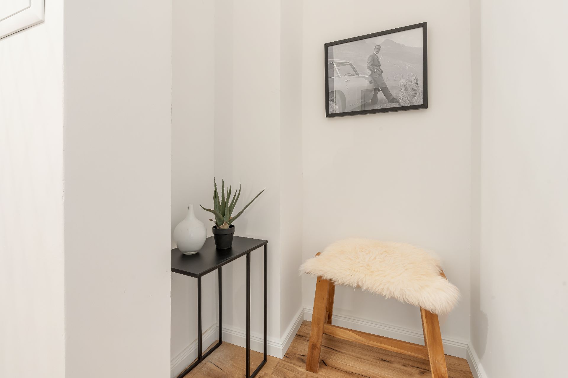 Kleine Ecke mit Hocker, Fellauflage, Beistelltisch, Pflanze und Bild an weißer Wand.