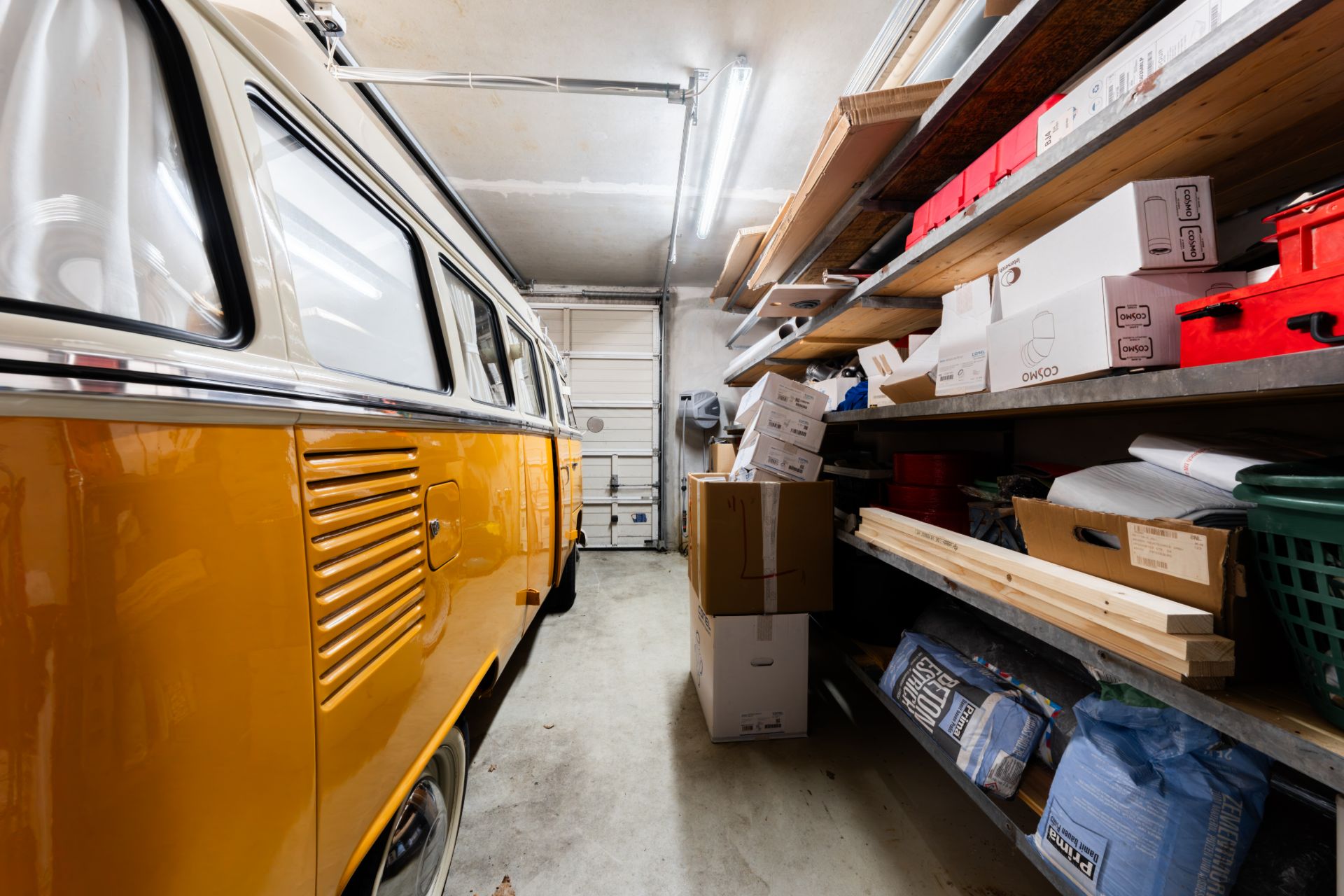 Garage mit gelbem Oldtimer-Bus und Regalen voller Kartons und Werkzeug.
