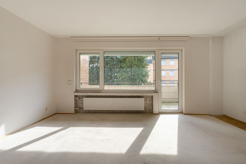 Leeres, helles Zimmer mit großem Fenster, Heizung und Zugang zu einem Balkon.