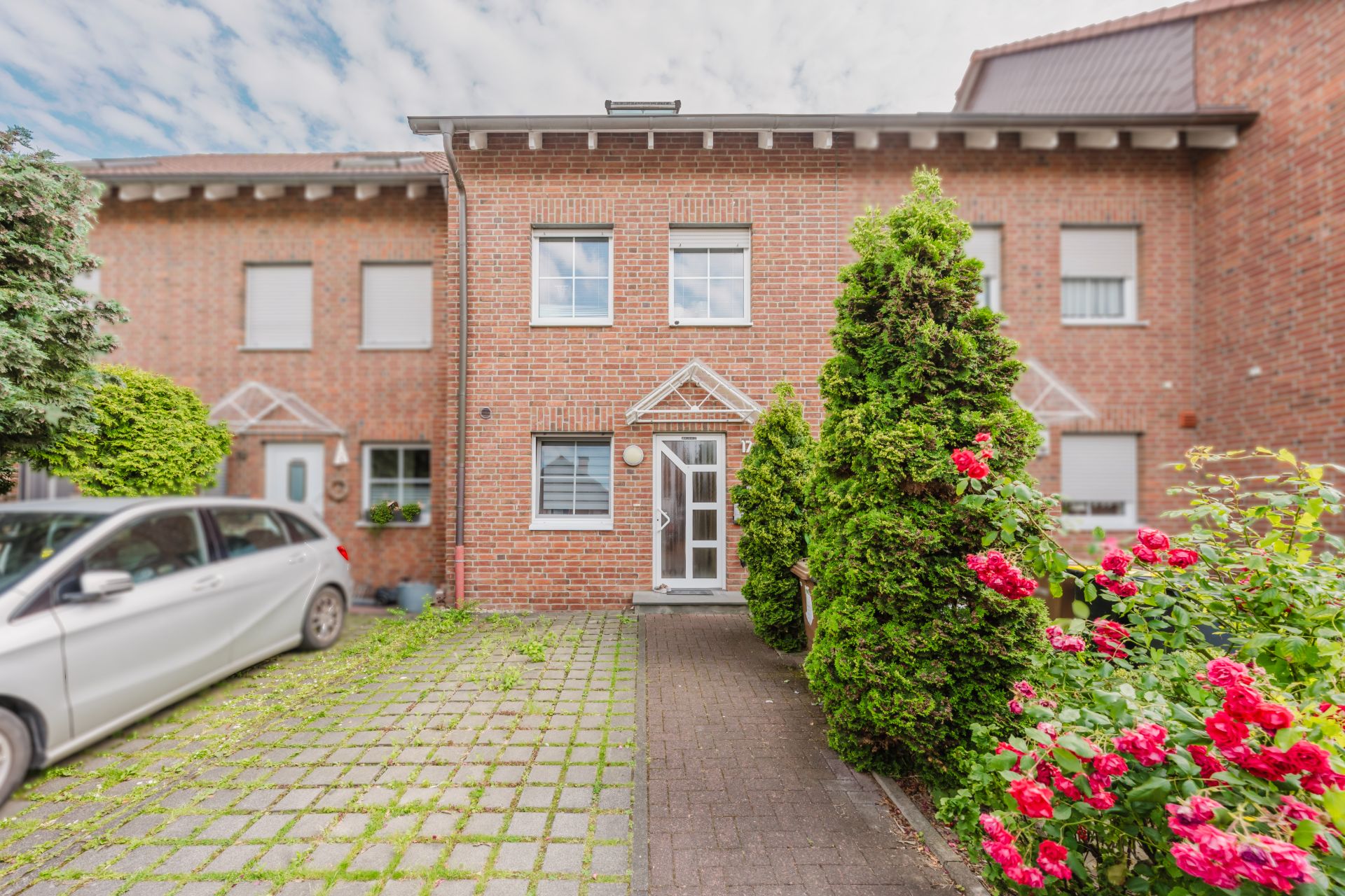 Vorderansicht eines Reihenhauses mit Eingang, Auto und Blumen im Vorgarten.