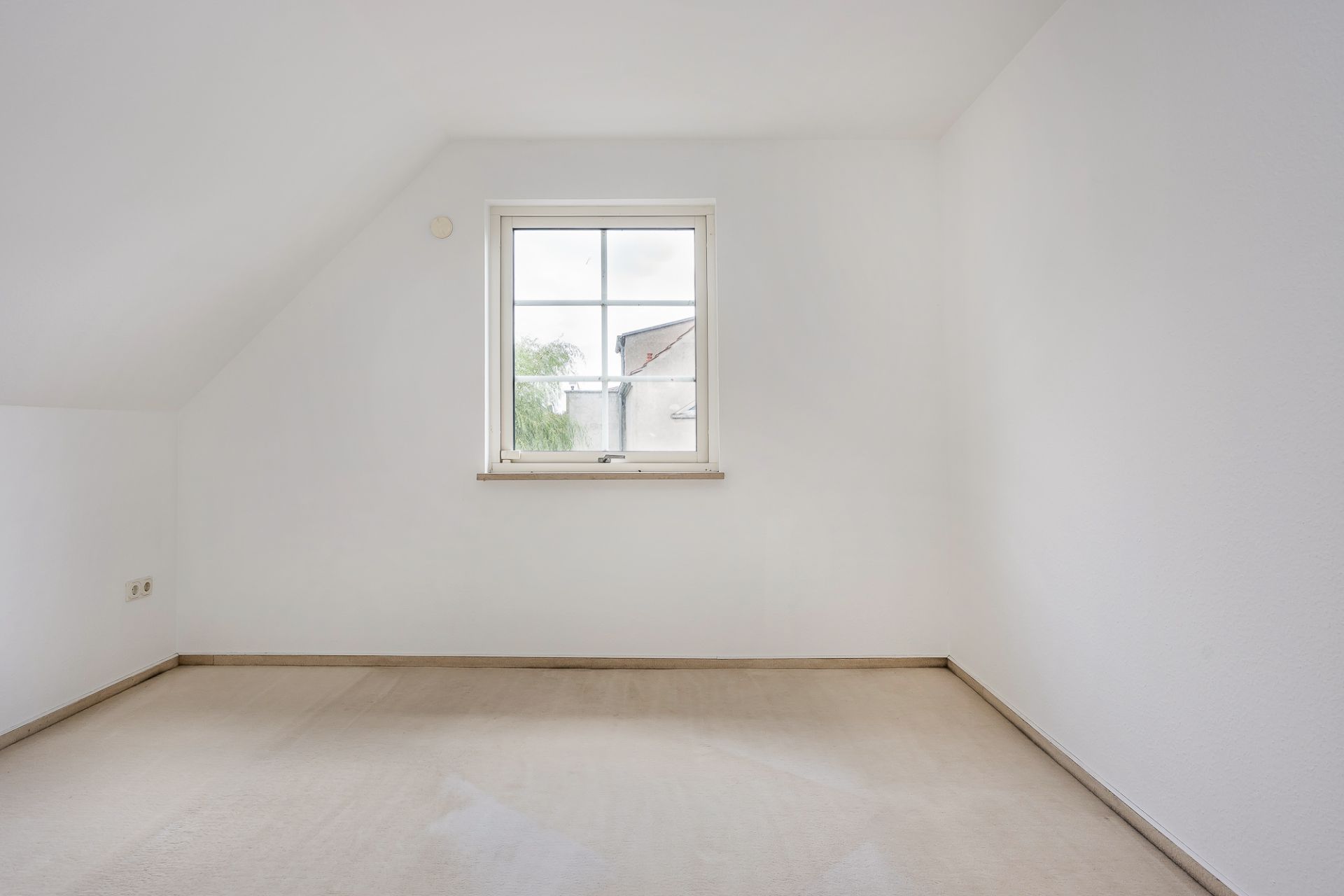 Leeres Zimmer mit weiß gestrichenen Wänden und einem Fenster mittig an der Stirnwand.