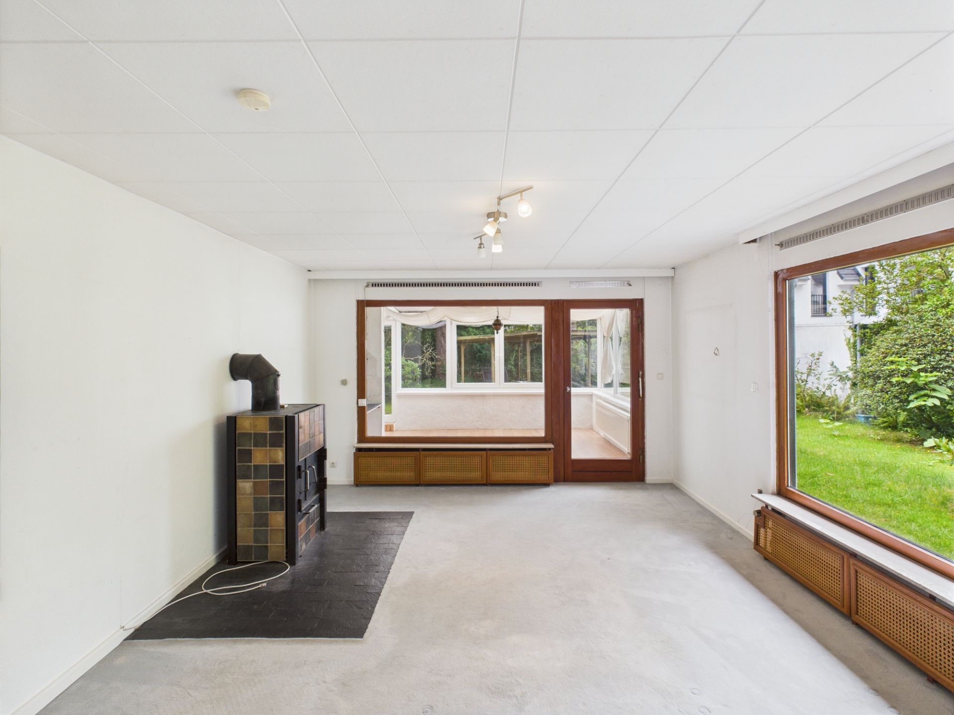 Helles Wohnzimmer mit Kaminofen und großen Fenstern zum Garten.