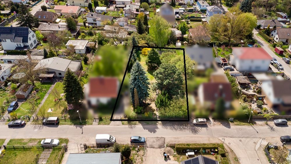 Luftaufnahme eines eingezäunten Grundstücks mit vielen Bäumen und zwei Straßen mit Autos davor.