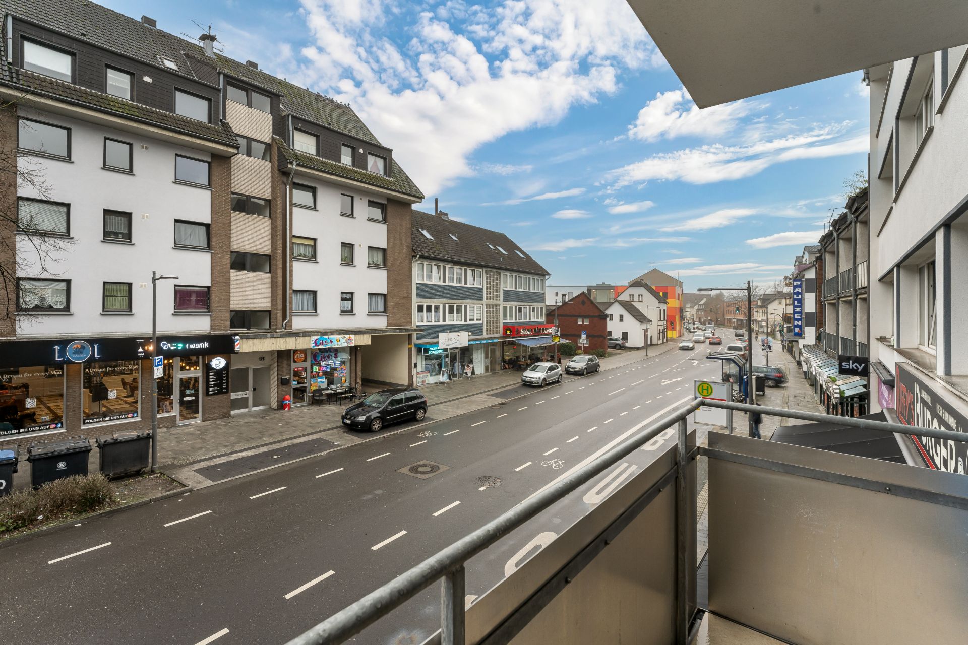 Blick von einem Balkon auf eine belebte Straße mit Geschäften und Wohnungen.