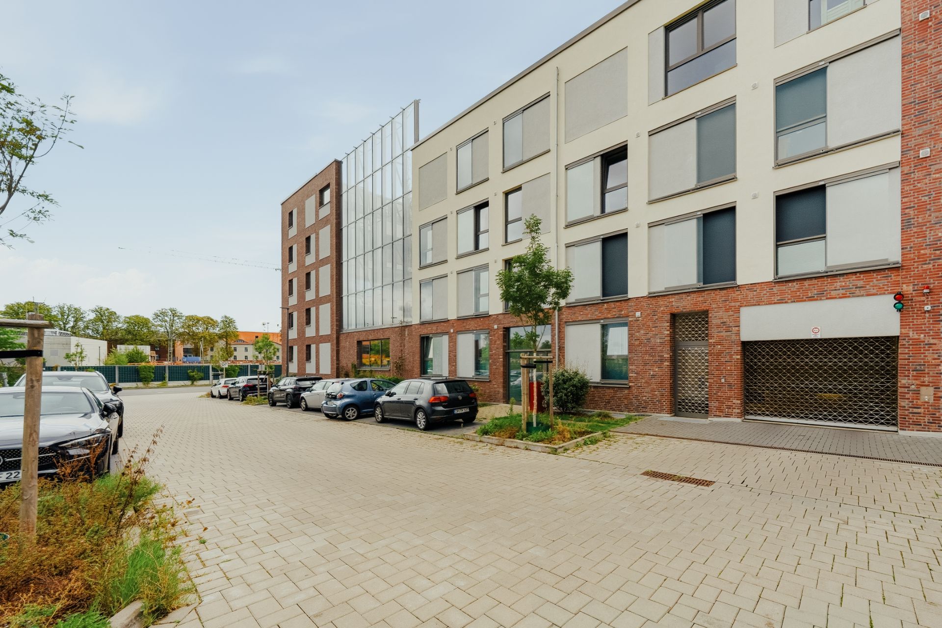 Mehrstöckiges Wohngebäude mit geparkten Autos auf einem gepflasterten Parkplatz.
