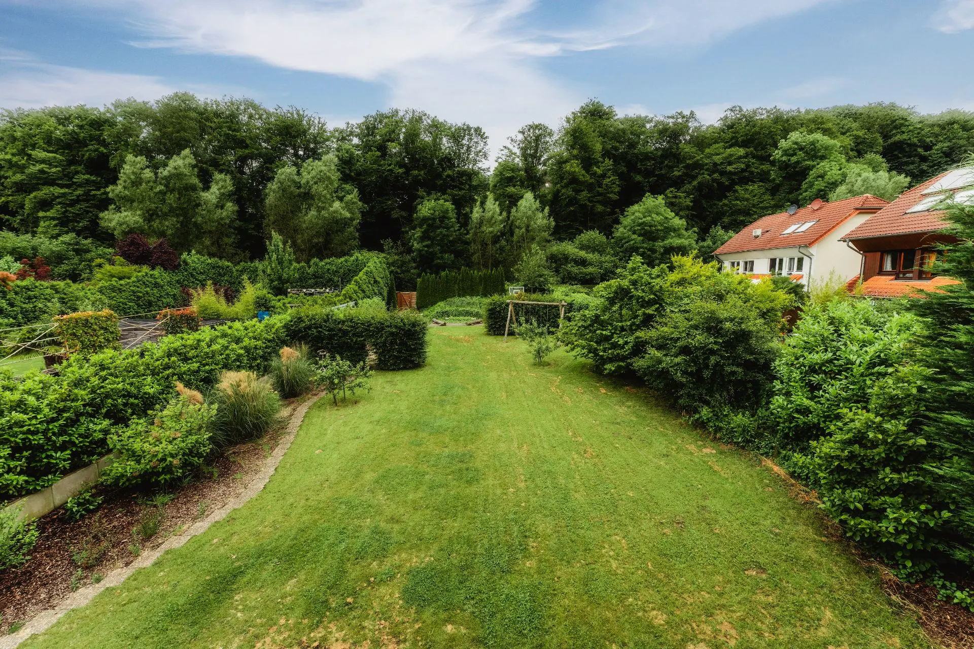 Großer Garten mit Rasen, Sträuchern und Bäumen. Im Hintergrund sind Wohnhäuser sichtbar.