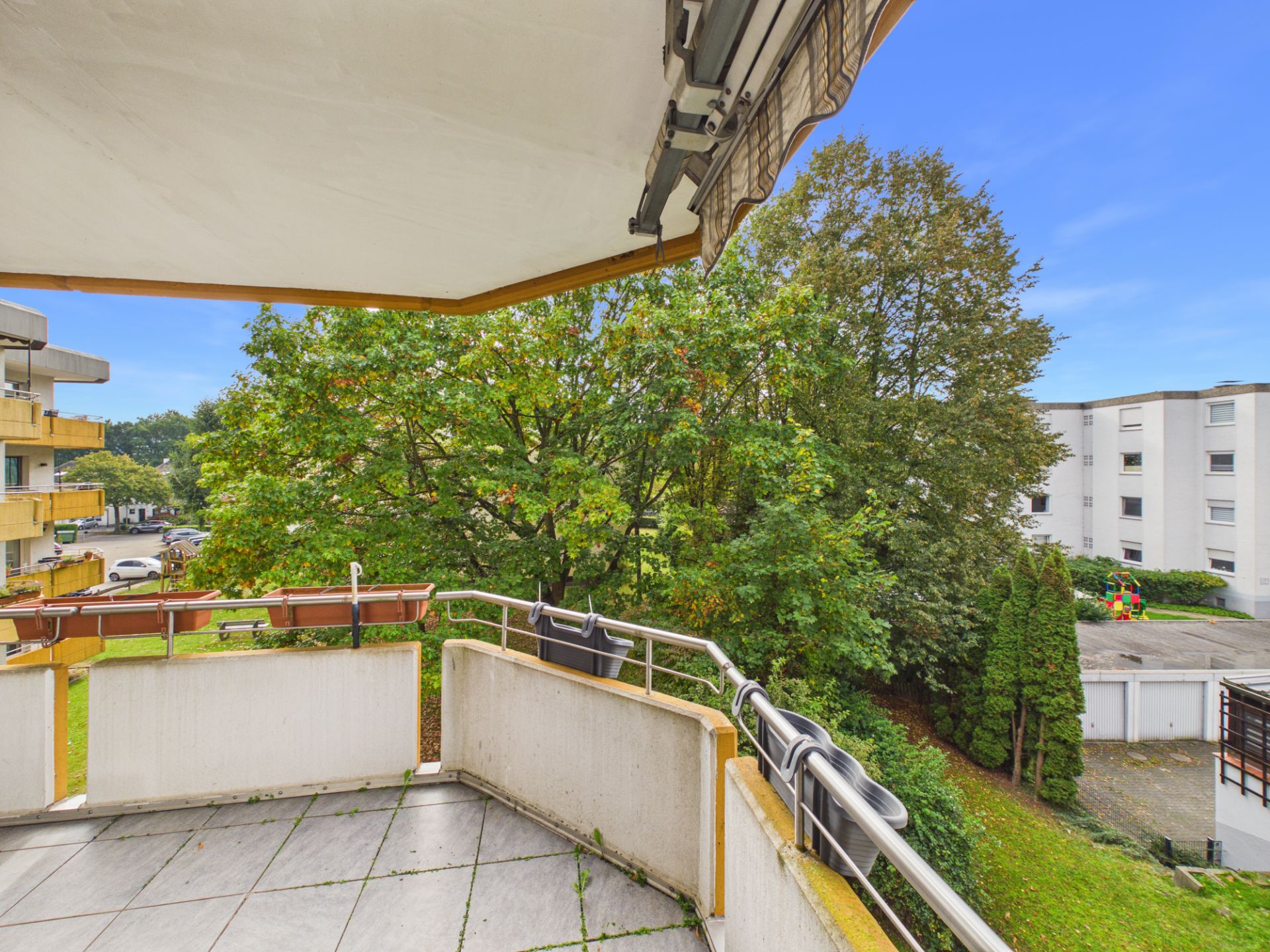 Balkon mit Markise, Blick auf Bäume und angrenzende Wohngebäude.