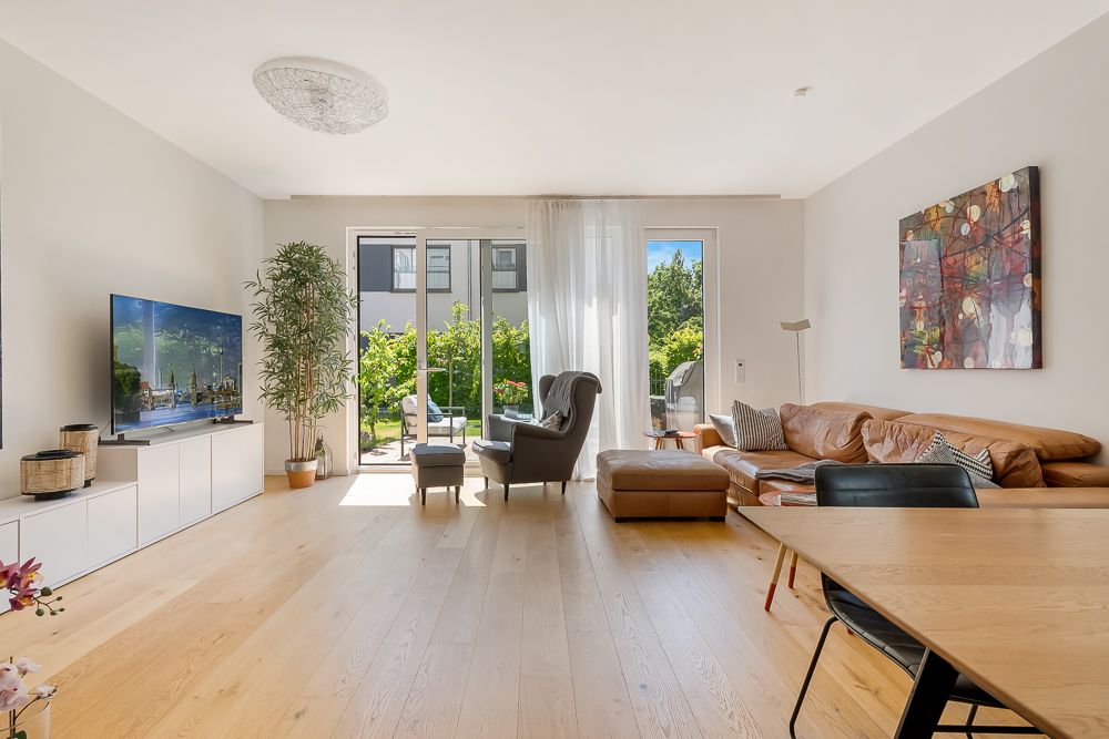 Helles Wohnzimmer mit Holzboden, Ledersofa, Sessel, Fernseher und Zugang zur Terrasse.