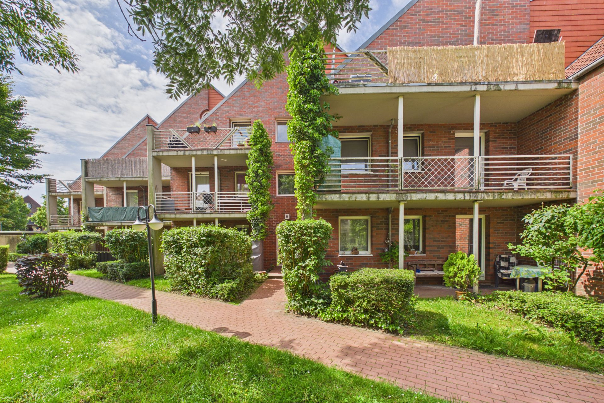 Mehrfamilienhaus aus rotem Backstein mit Balkonen und gepflegtem Gartenweg im Vordergrund.