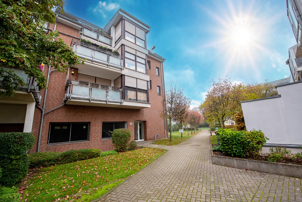 Mehrfamilienhaus mit Balkonen, Vorgarten und Gehweg bei sonnigem Wetter.