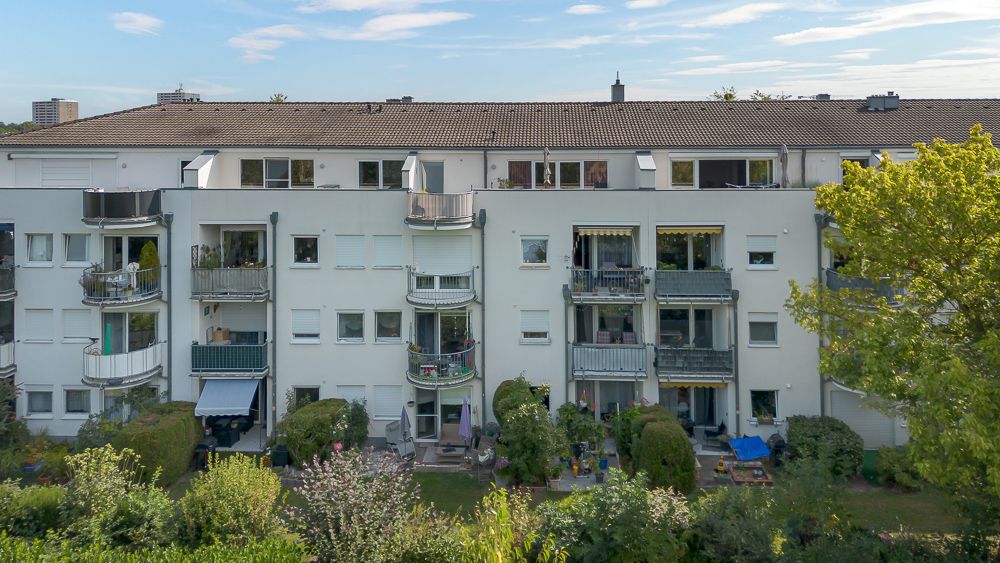 Mehrstöckiges Wohnhaus mit Balkonen und begrünter Gartenanlage davor.