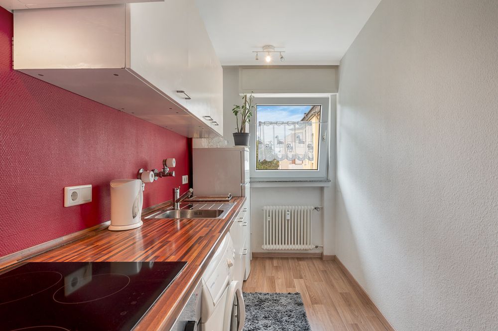 Schmale Küche mit roter Wand, Holzarbeitsplatte, Herd, Spüle und Fenster am Ende des Raums.
