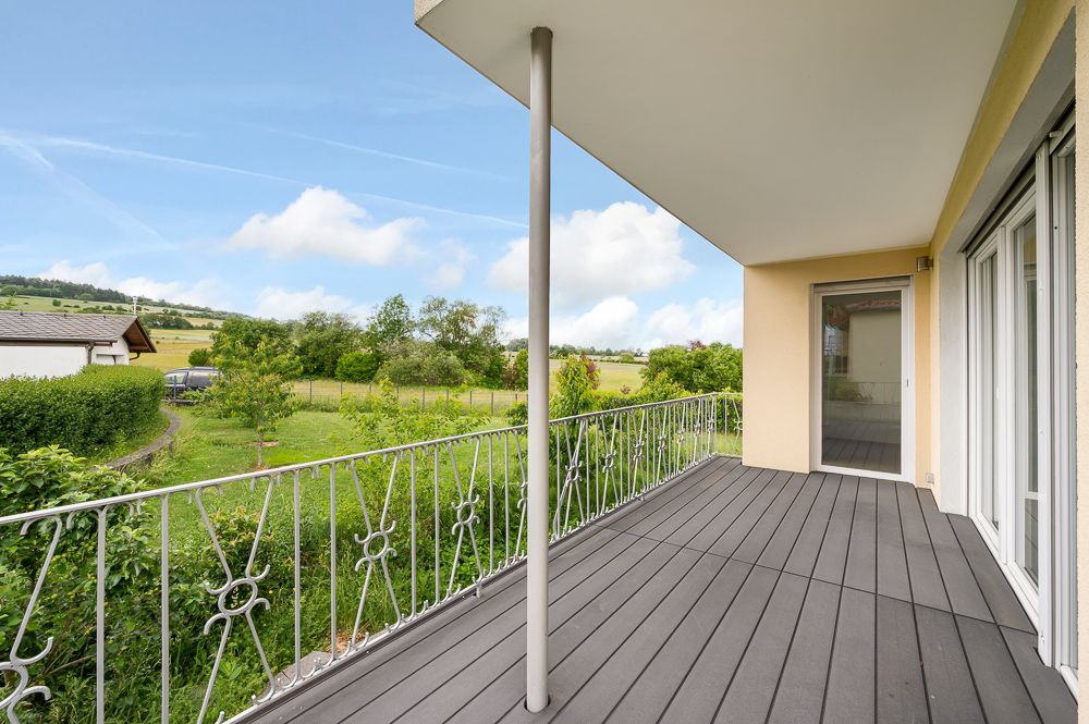 Balkon mit Metallgeländer, Blick auf Garten und Wiese, Zugang durch Glastür.