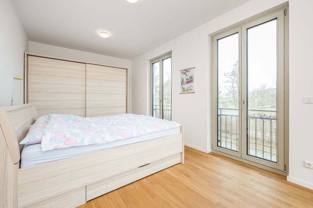 Helles Schlafzimmer mit Doppelbett, großem Kleiderschrank und zwei bodentiefen Fenstern.