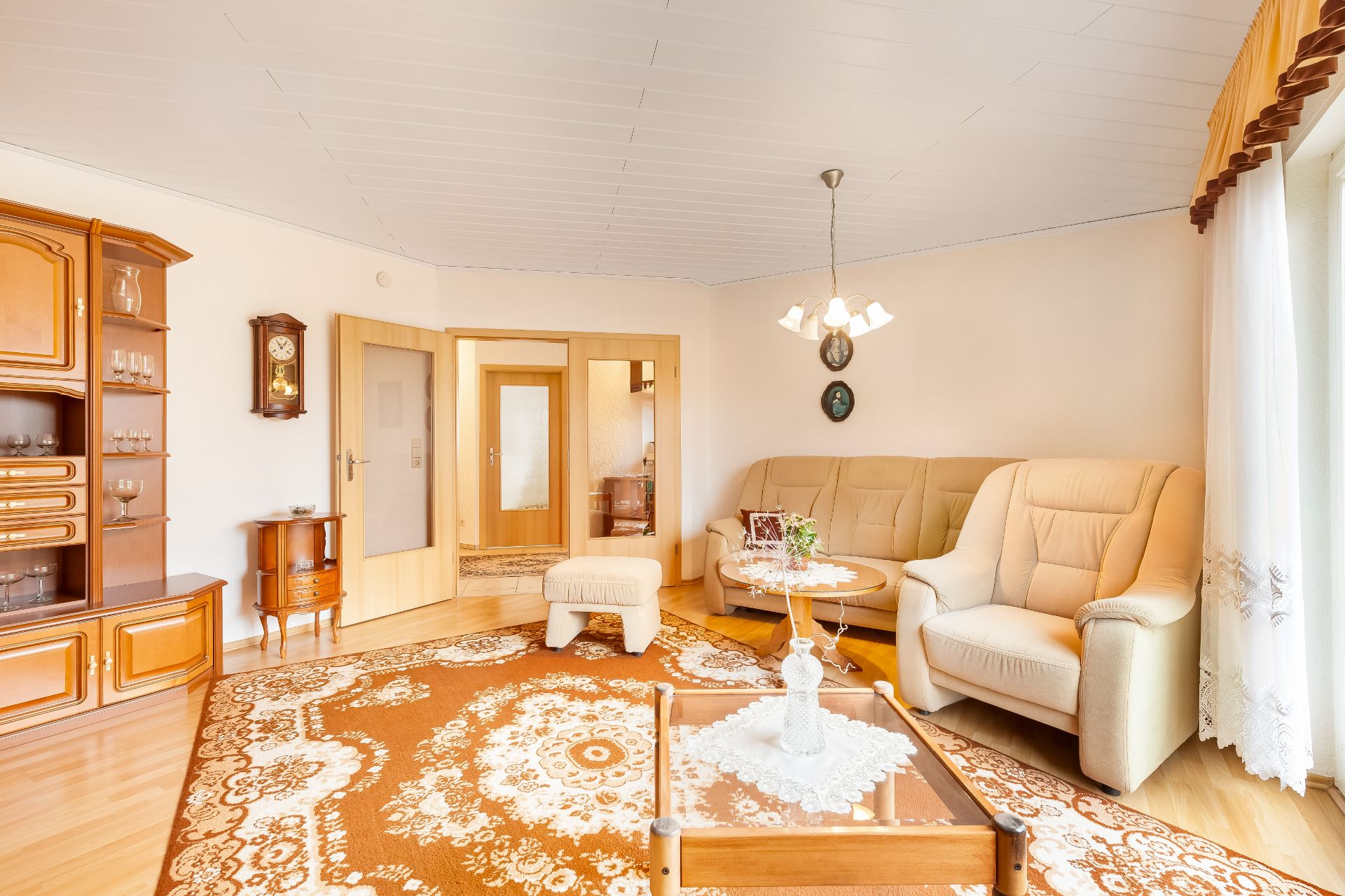 Helles Wohnzimmer mit beiger Sitzgruppe, Holzmöbeln und gemustertem Teppich.