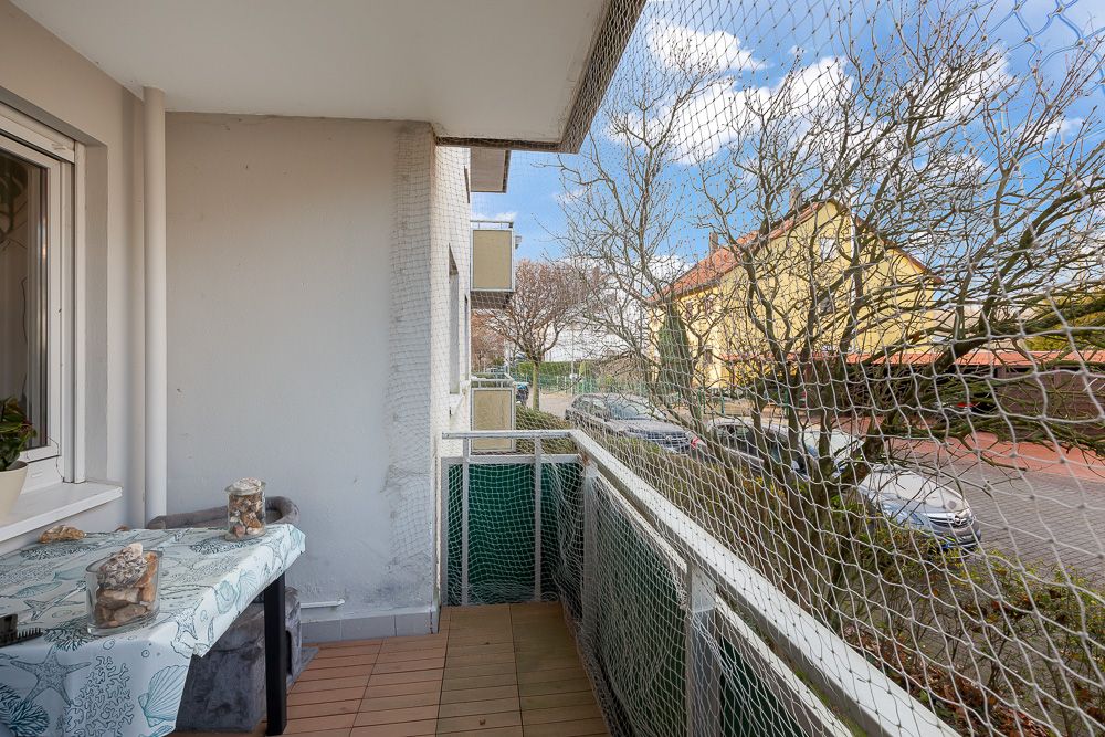 Balkon mit Netz, Tisch und Dekoration, mit Blick auf eine ruhige Straße und Bäume.