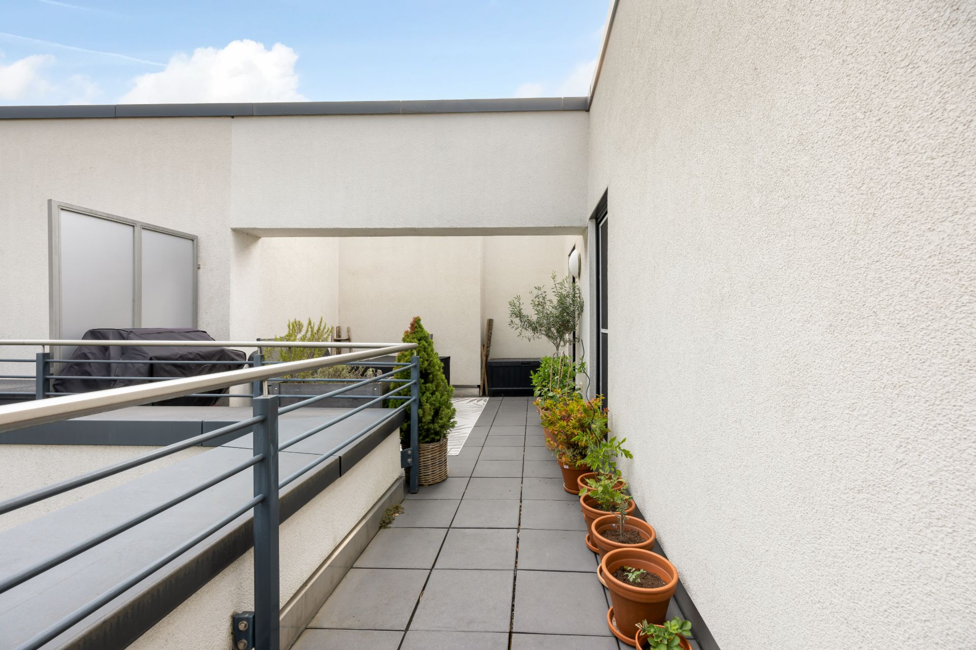 Moderne Dachterrasse mit Topfpflanzen am Rand und einem Grill auf der linken Seite.