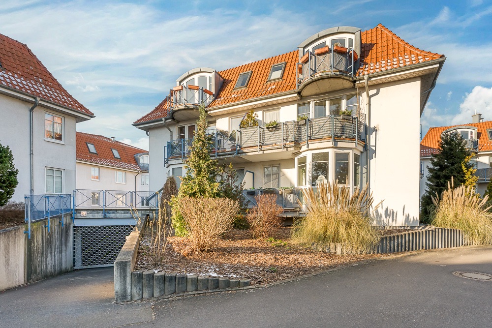 Modernes Wohnhaus mit roten Dachziegeln, Balkonen und gepflegtem Vorgarten.