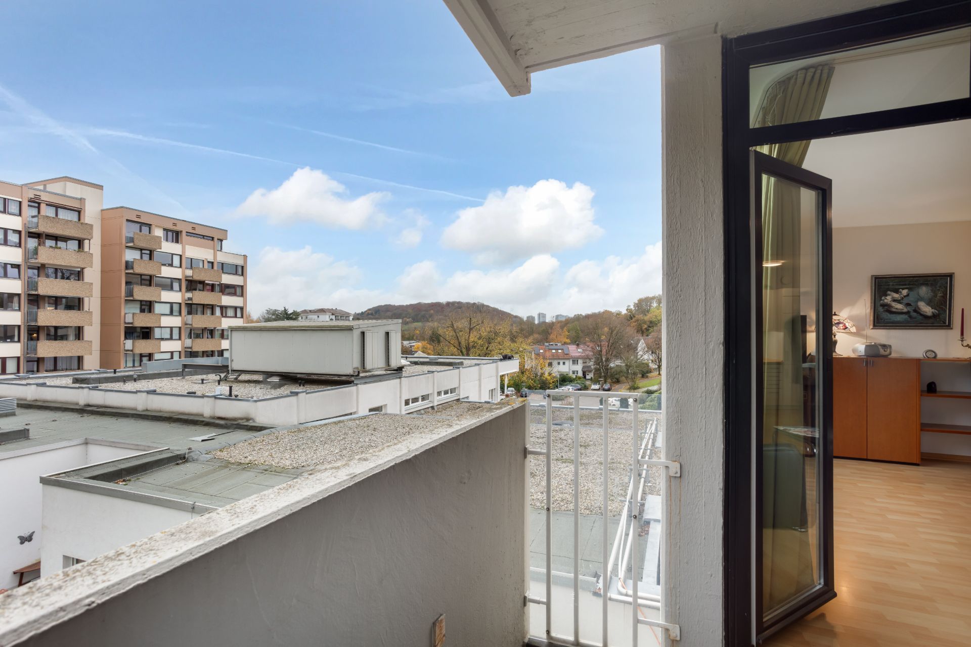 Blick von einem Balkon auf Nachbargebäude, mit offenem Zugang zu einem Wohnzimmer.