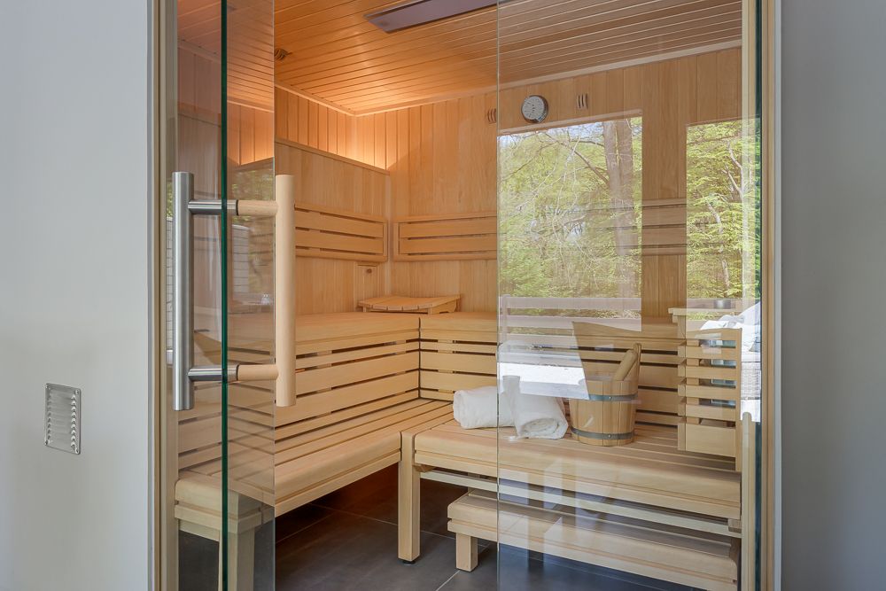 Moderne Holzsauna mit Glaswand, Handtüchern und Eimer auf der Bank.