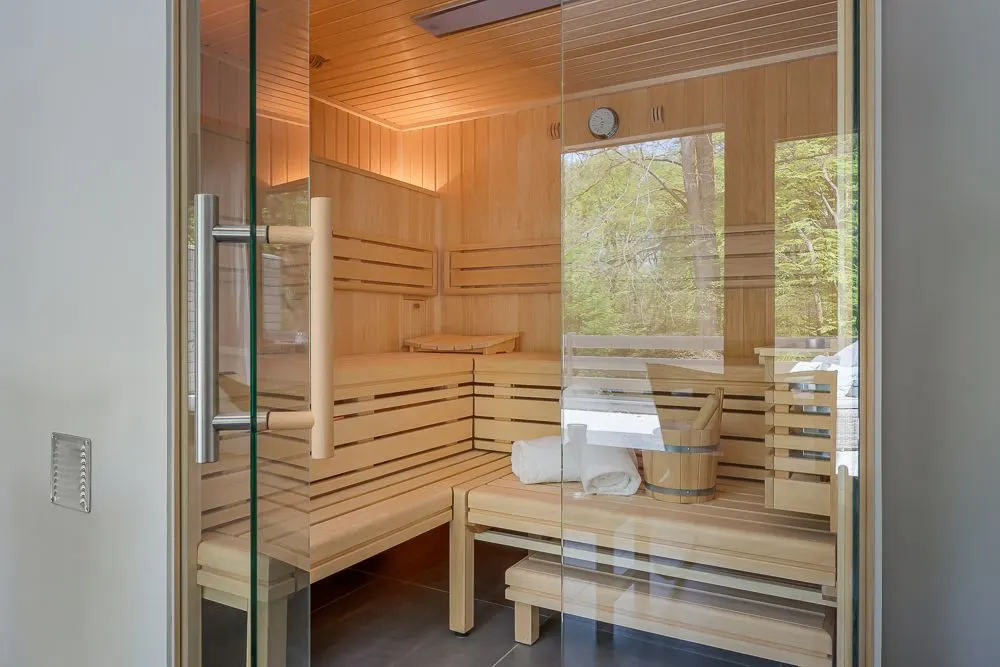Moderne Holzsauna mit Glaswand, Handtüchern und Eimer auf der Bank.