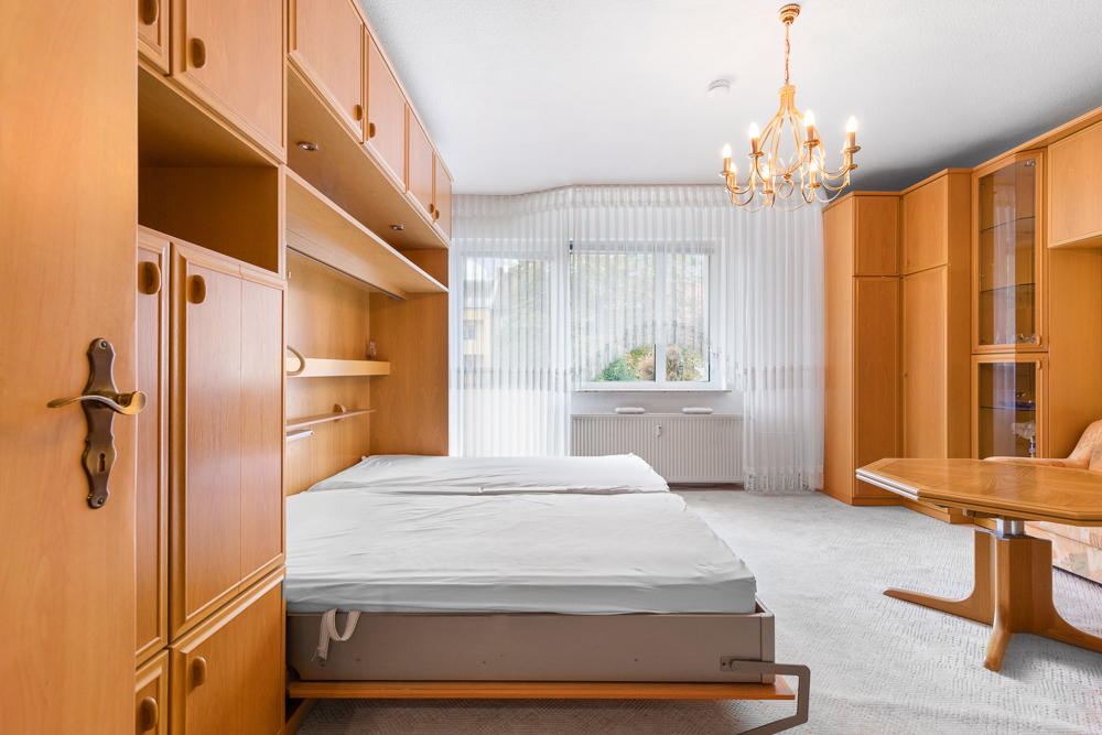 Schlafzimmer mit Holzschränken, Doppelbett, großem Fenster und Kronleuchter.