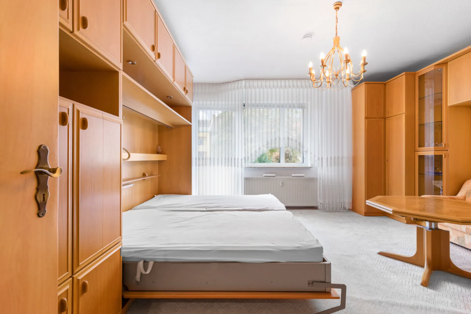 Schlafzimmer mit Holzschränken, Doppelbett, großem Fenster und Kronleuchter.