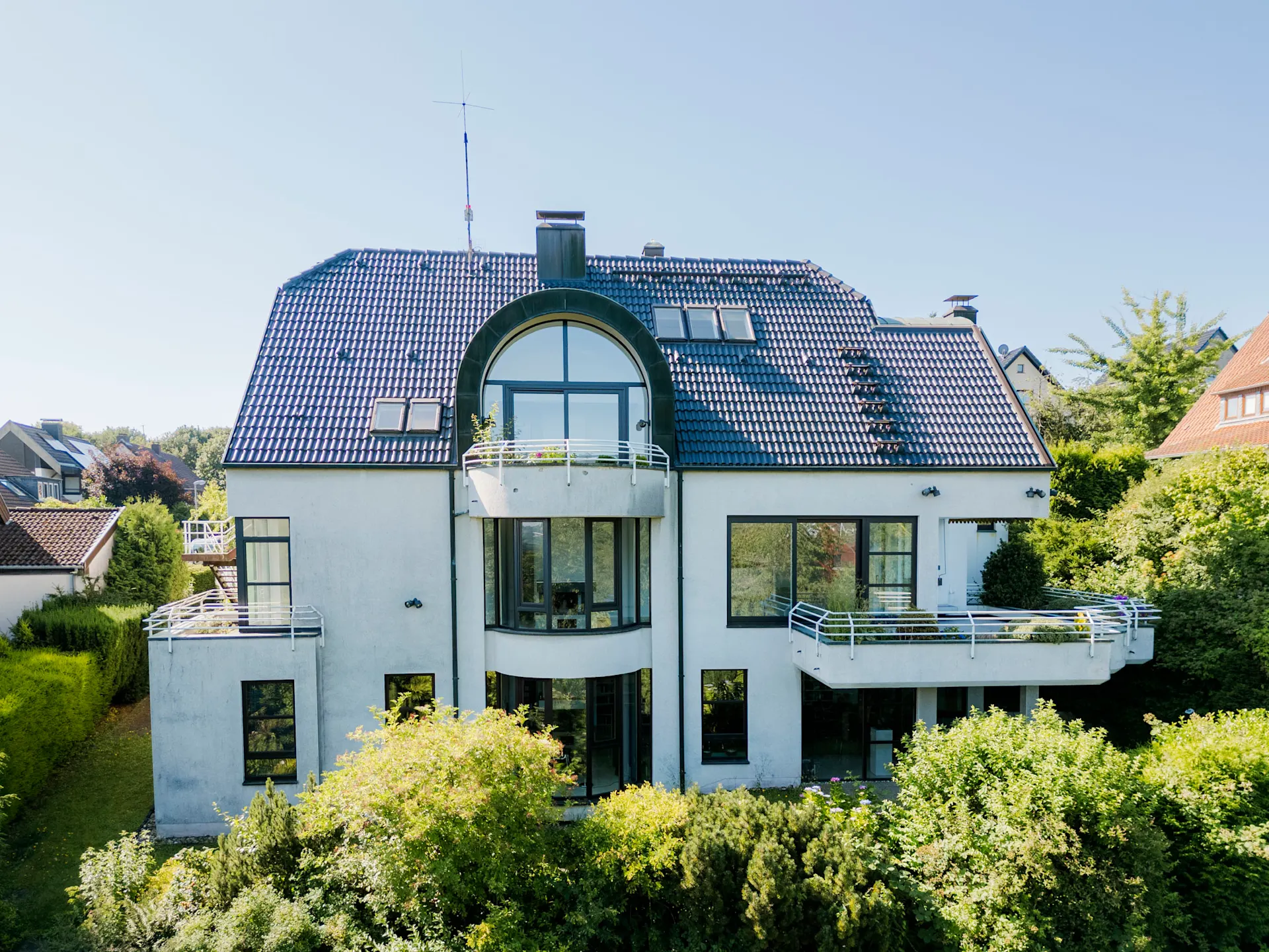 Großes, modernes Wohnhaus mit blauer Dachziegeln, Balkonen und Garten im Vordergrund.