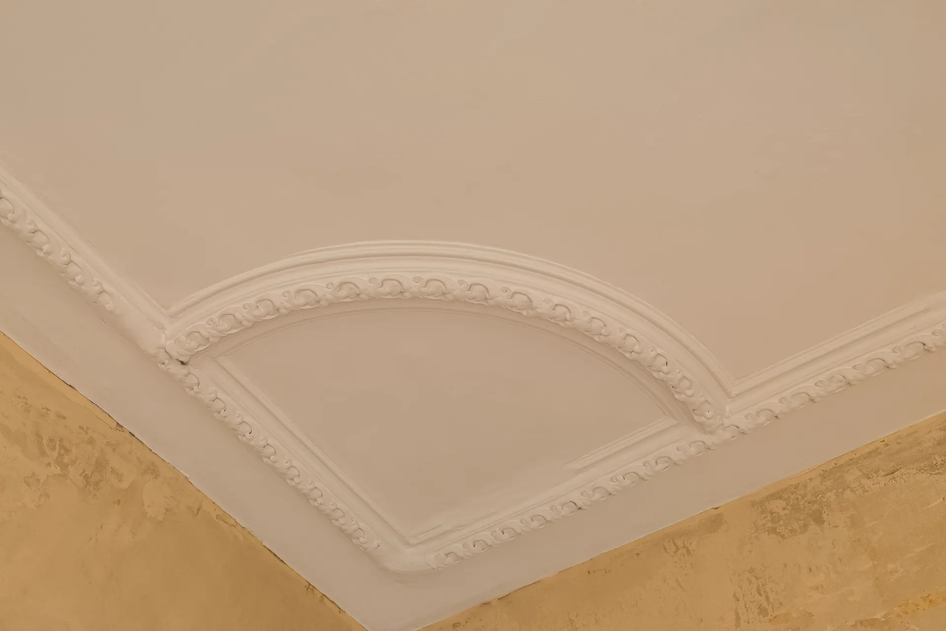 Stuckverzierung an einer weißen Zimmerdecke in einer Ecke, mit beigem Rand an der Wand.