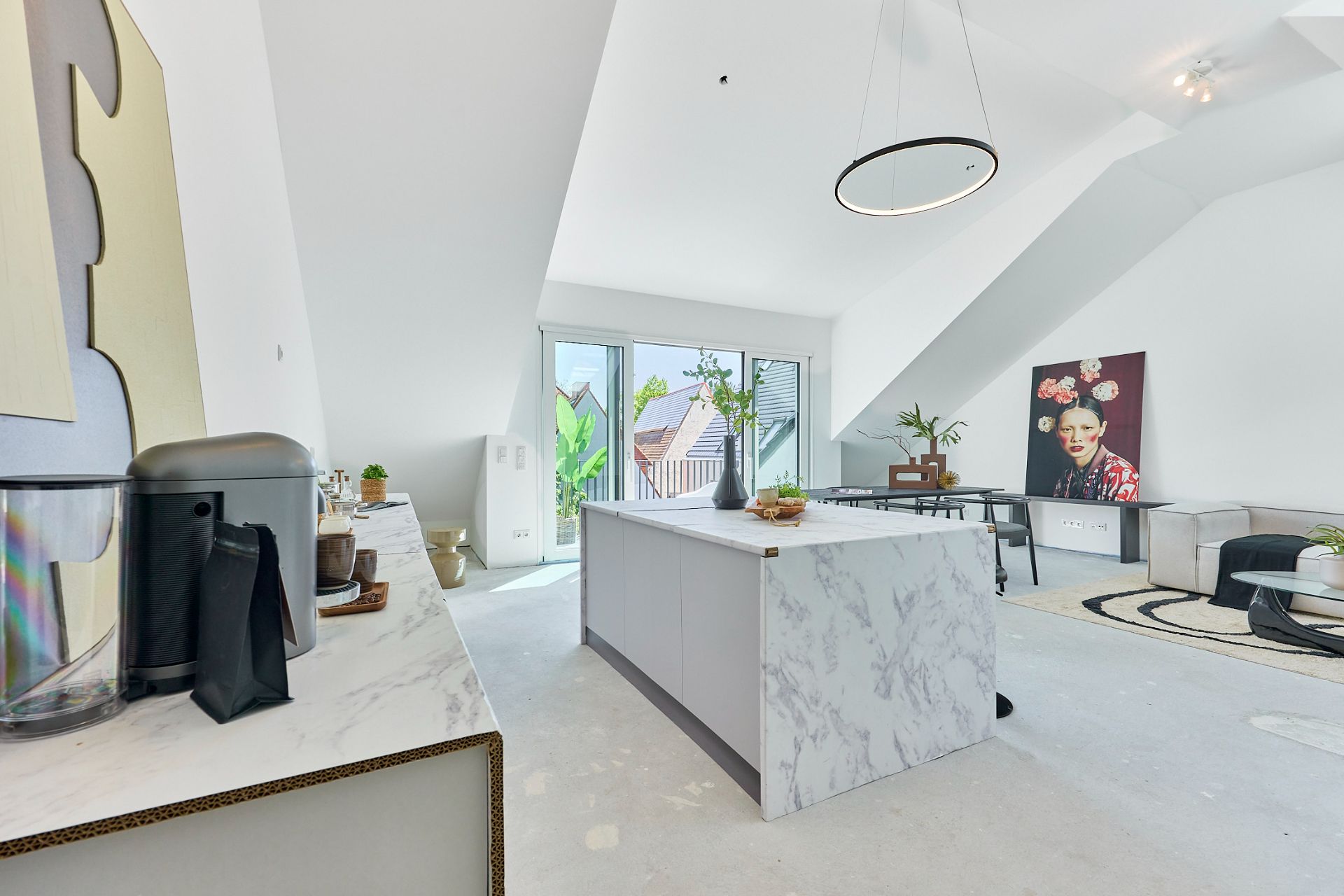 Helle, moderne Wohnküche mit Kücheninsel und großem Fenster, Wohnzimmer im Hintergrund.